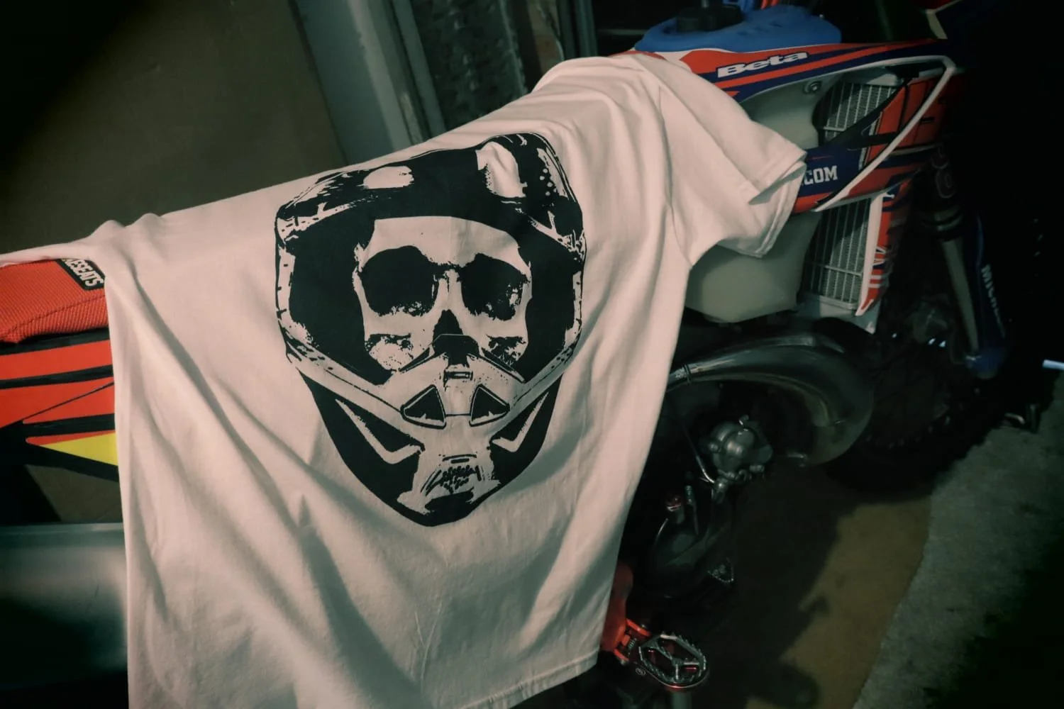 White moto skull graphic t shirt hangs on enduro bike in garage