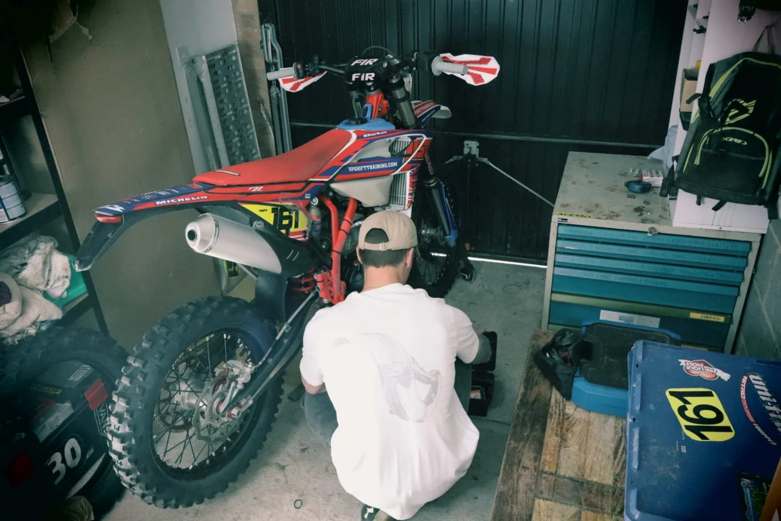 Man works on enduro motocross bike in garage wearing white 2 stroke graphic design t shirt