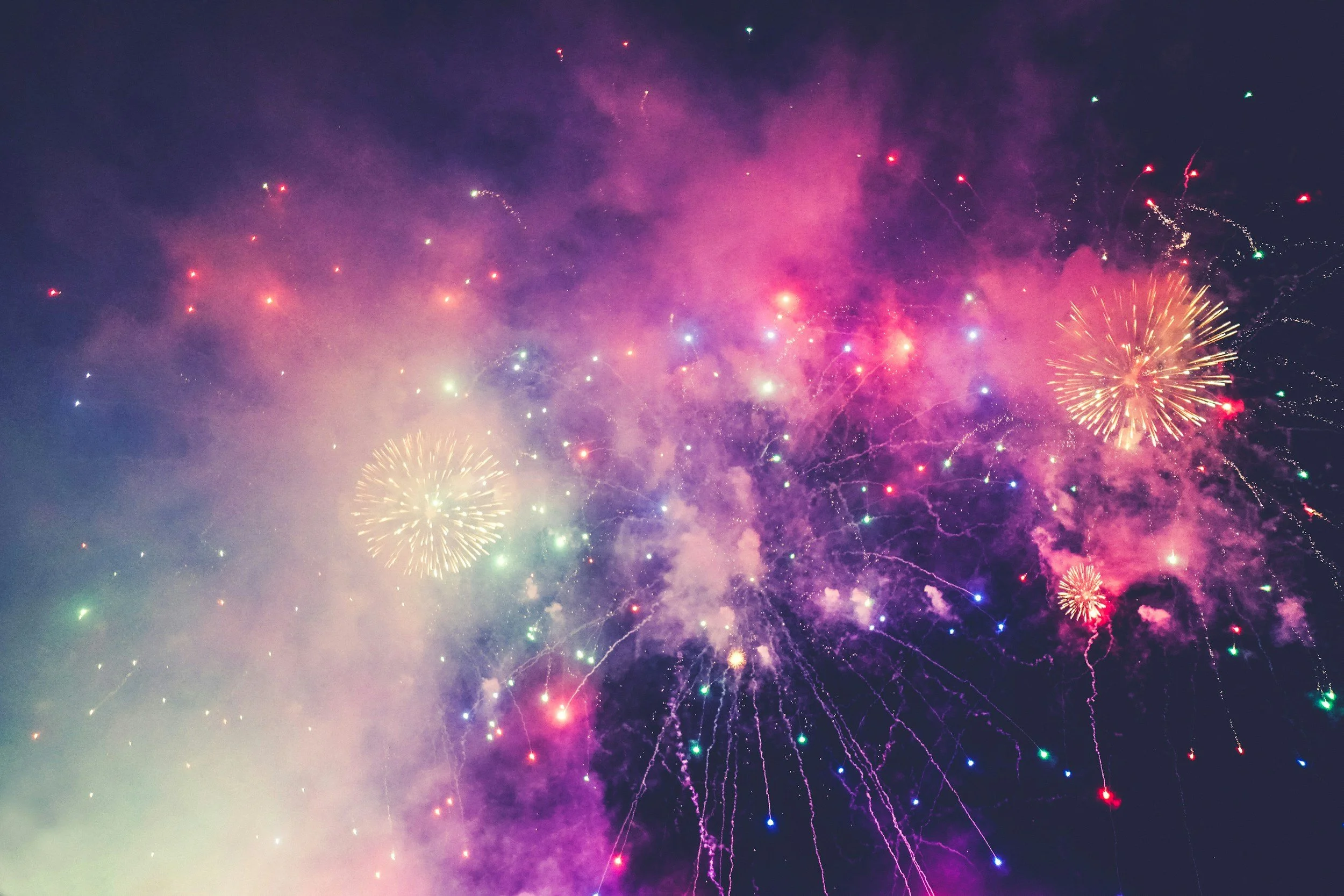Colorful fireworks illuminating the night sky with pink, purple, yellow, green, and blue hues.