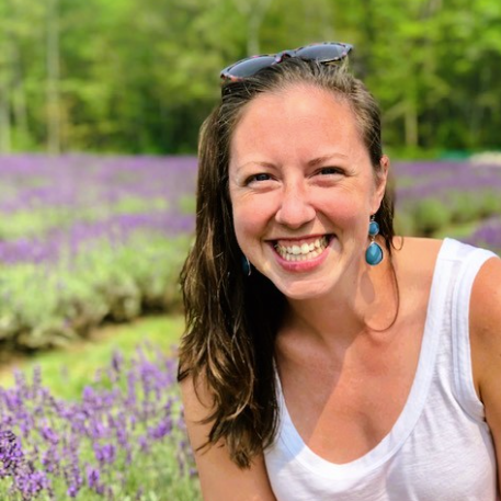A woman smiling outdoors with lavender fields in the background.