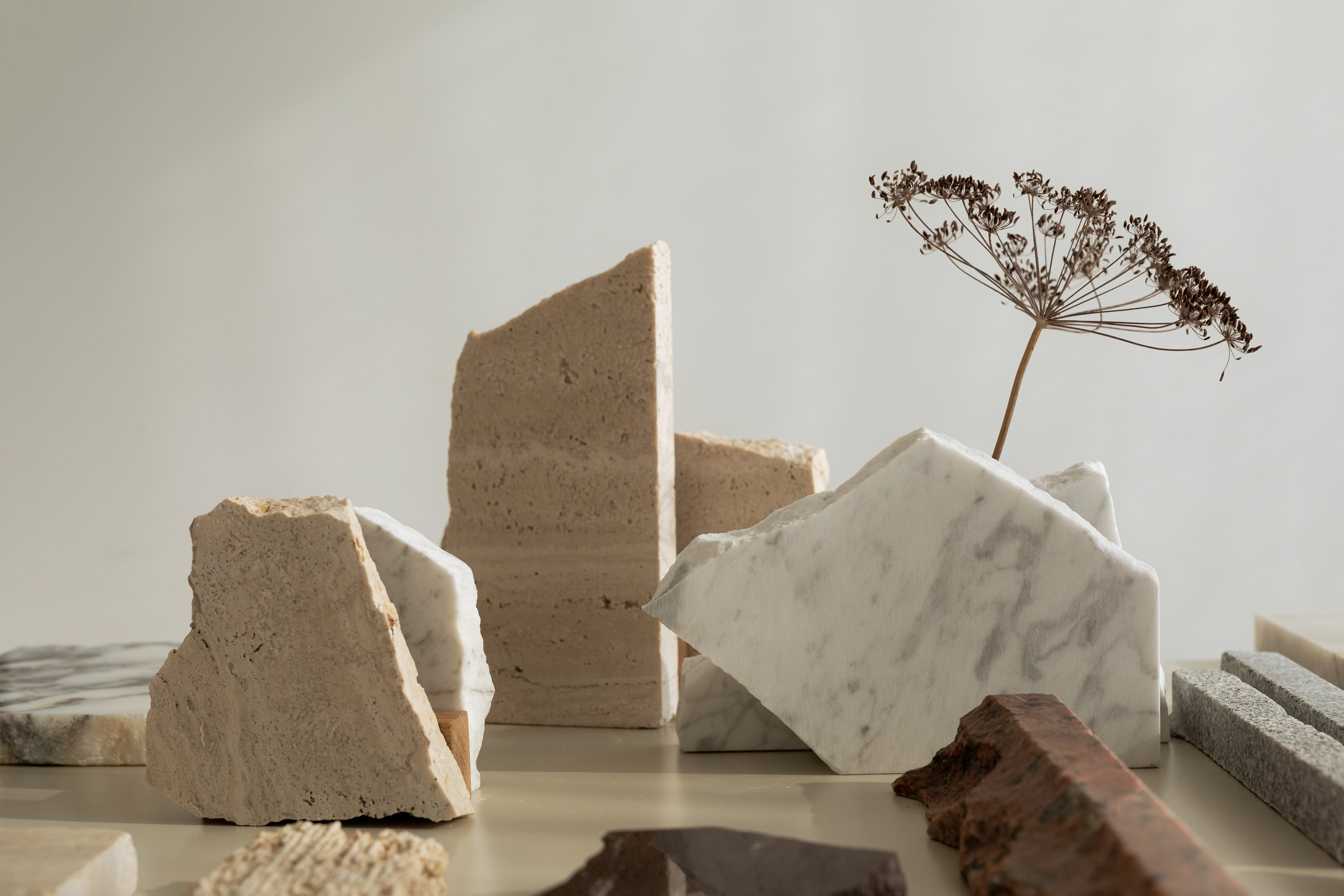 Various natural stone tiles and slabs arranged on a surface, with a dried plant in the background.