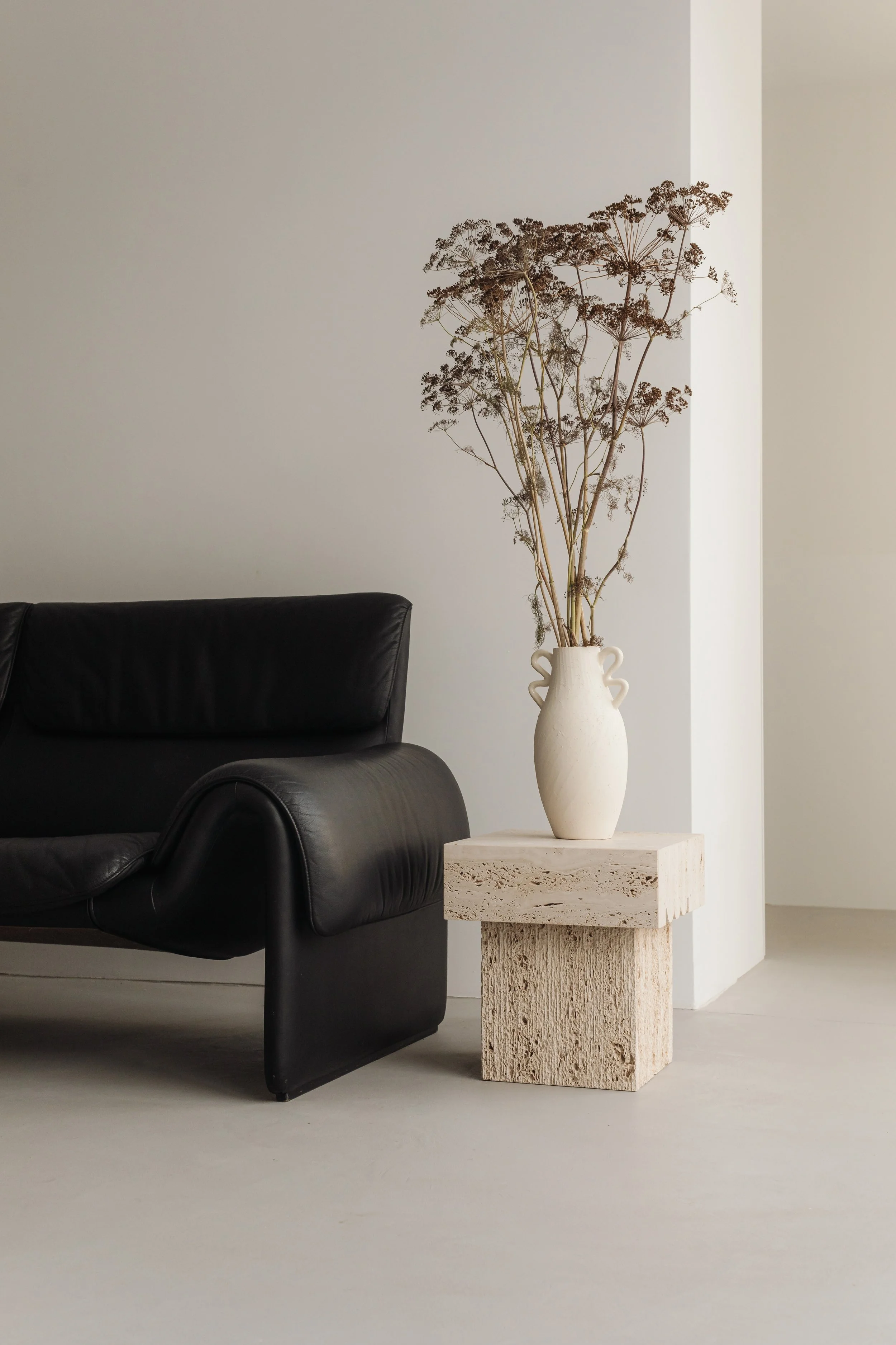 A black leather armchair next to a white marble side table with a beige ceramic vase holding dried flowers.