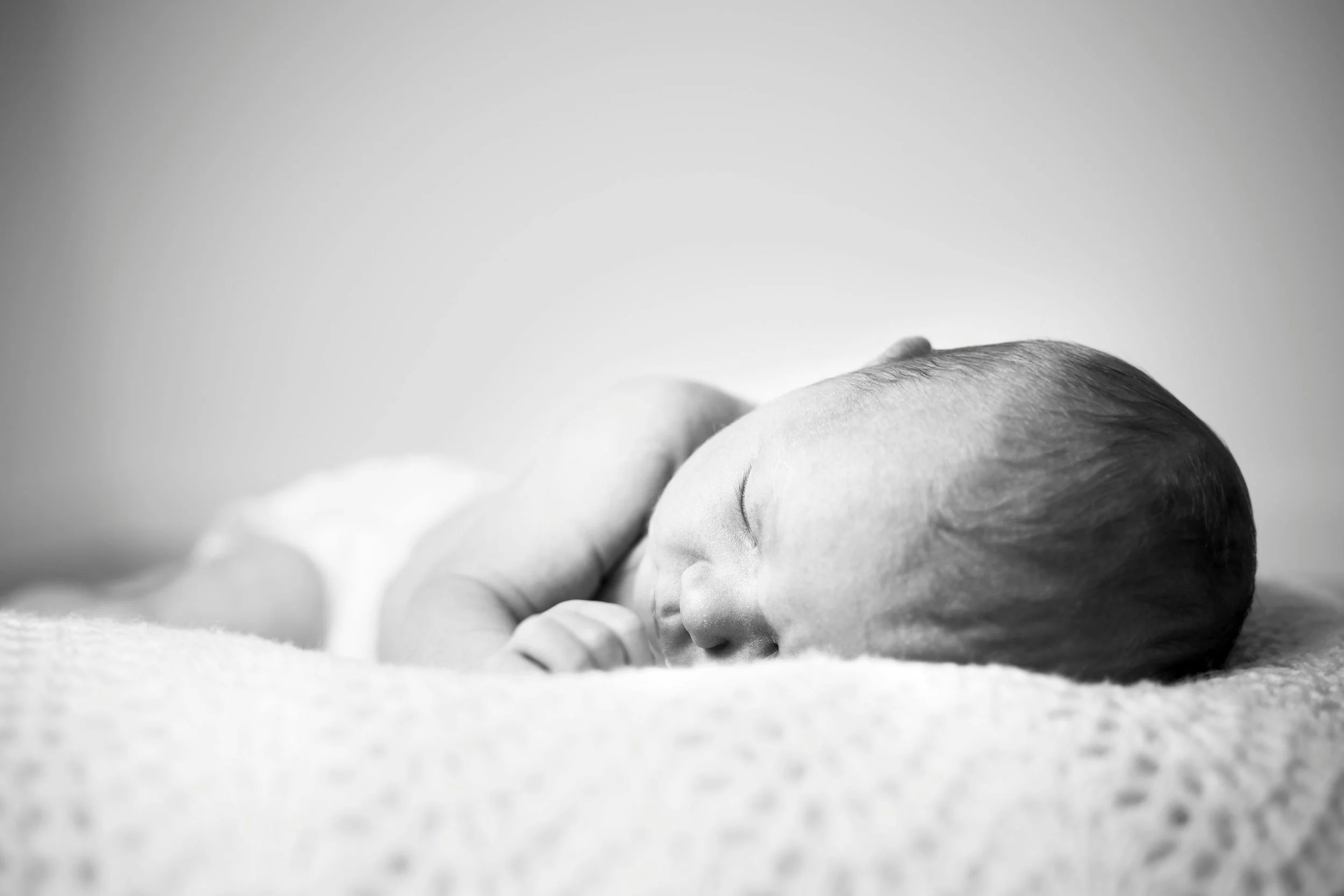 Close-up of a sleeping baby's face with peaceful expression, lying on a soft surface, in black and white.