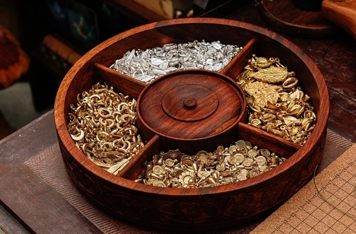 A round wooden jewelry box divided into four compartments, filled with assorted gold and silver jewelry pieces, such as chains, pendants, and charms.