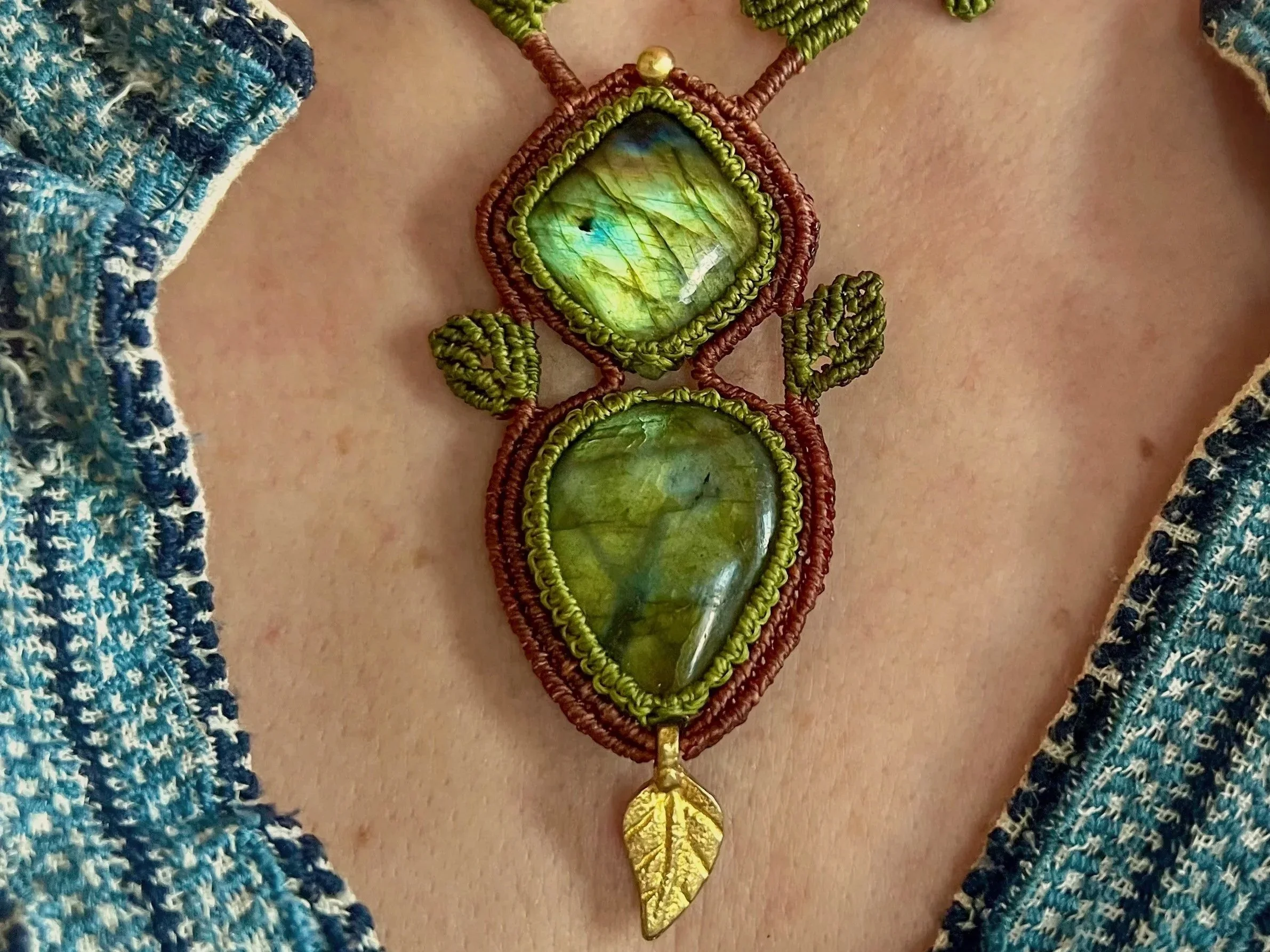 A close-up of a person wearing a handmade beaded necklace with three greenish gemstones and gold-colored leaf pendant.