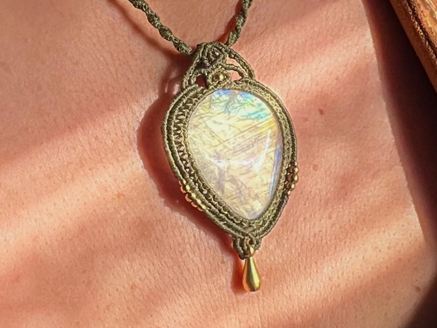 A person wearing a gold necklace with a large iridescent heart-shaped pendant hanging on their neck.