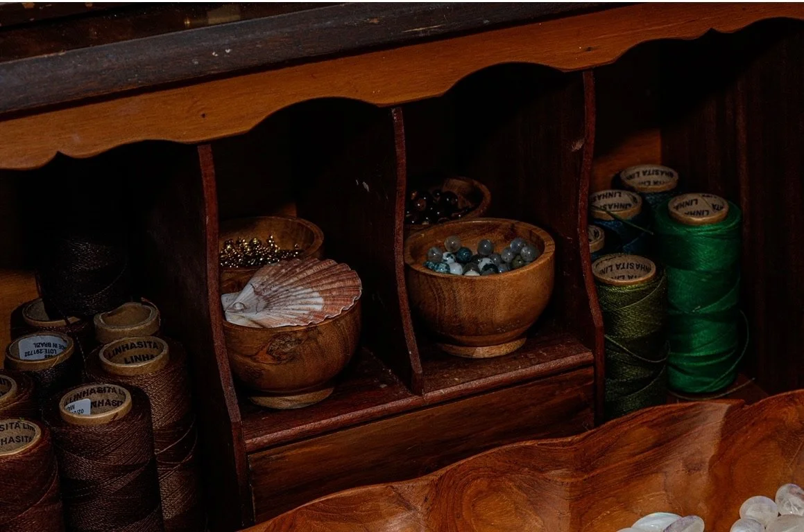 Wooden jewelry storage with spools of thread and bowls of beads and shells.
