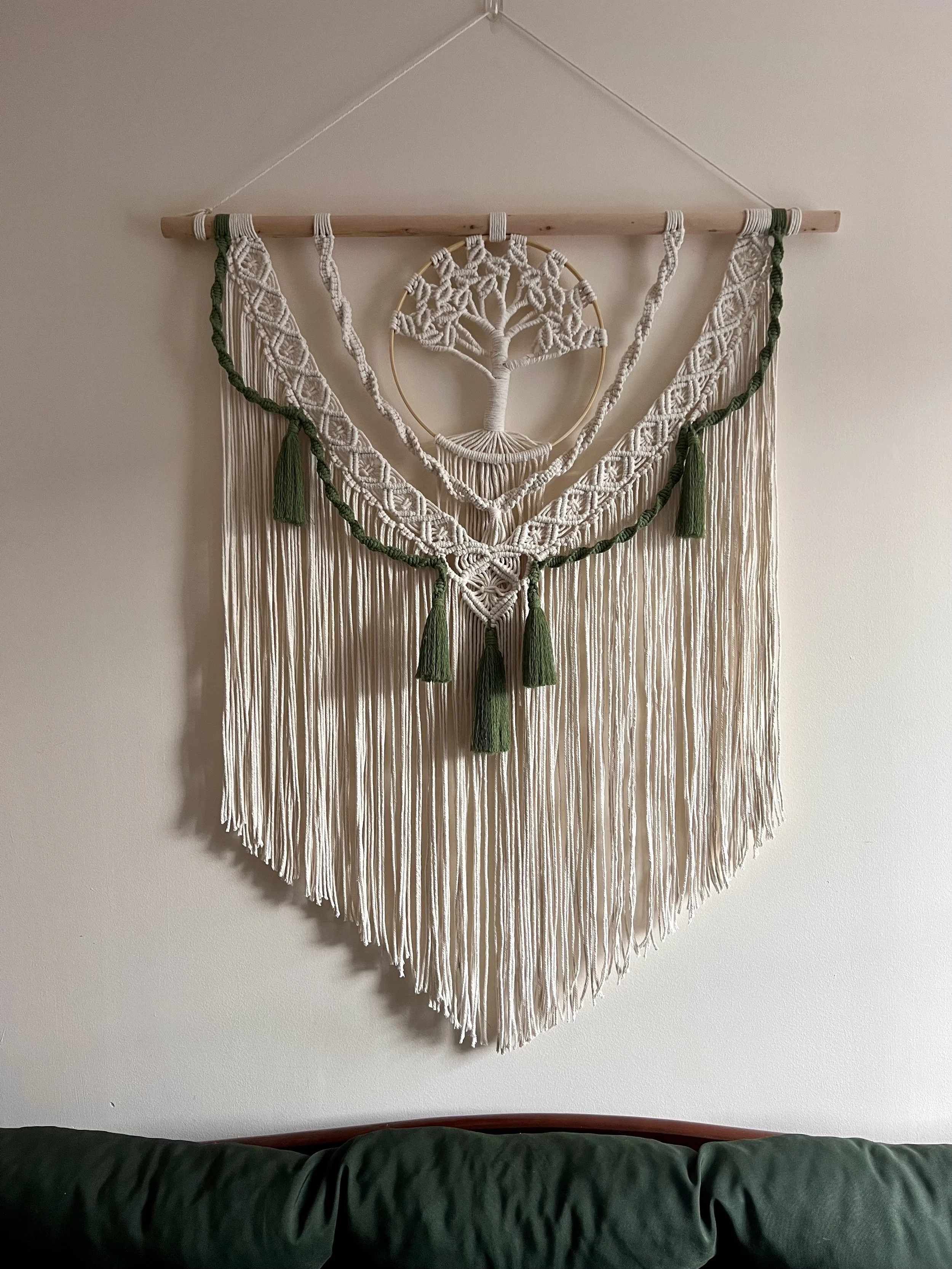 Wall hanging tapestry with a tree design, using white and green threads, featuring a circular element and long fringe hanging down.
