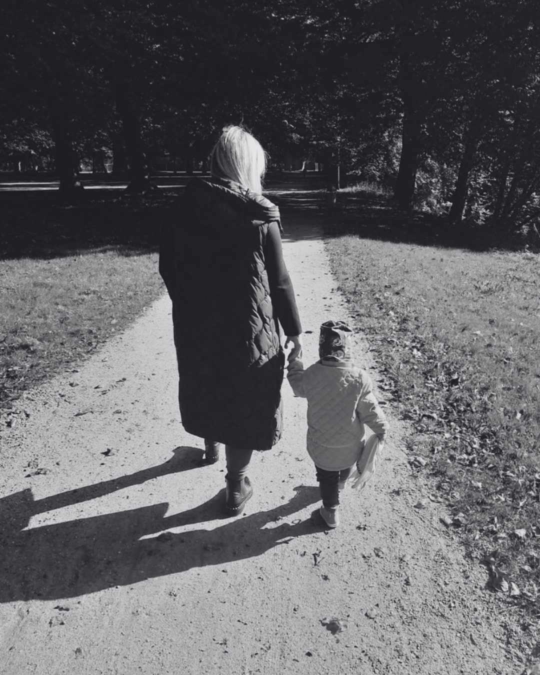 Frau geht Hand in Hand mit einem Kind einen Parkweg entlang – Schwarz-Weiß-Foto