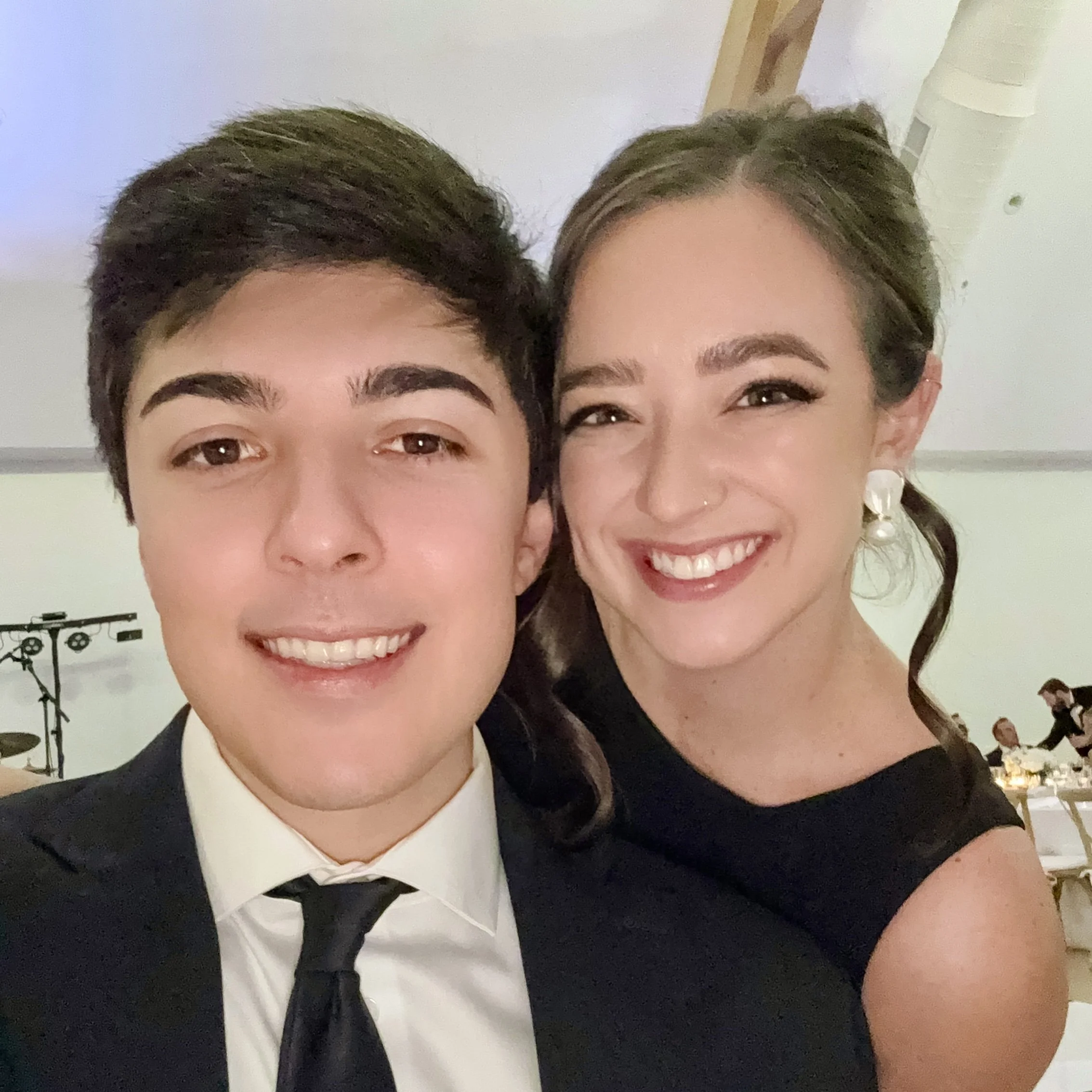Close-up of Claire and her boyfriend smiling, dressed formally, in an indoor setting with wood paneling and artwork in the background.