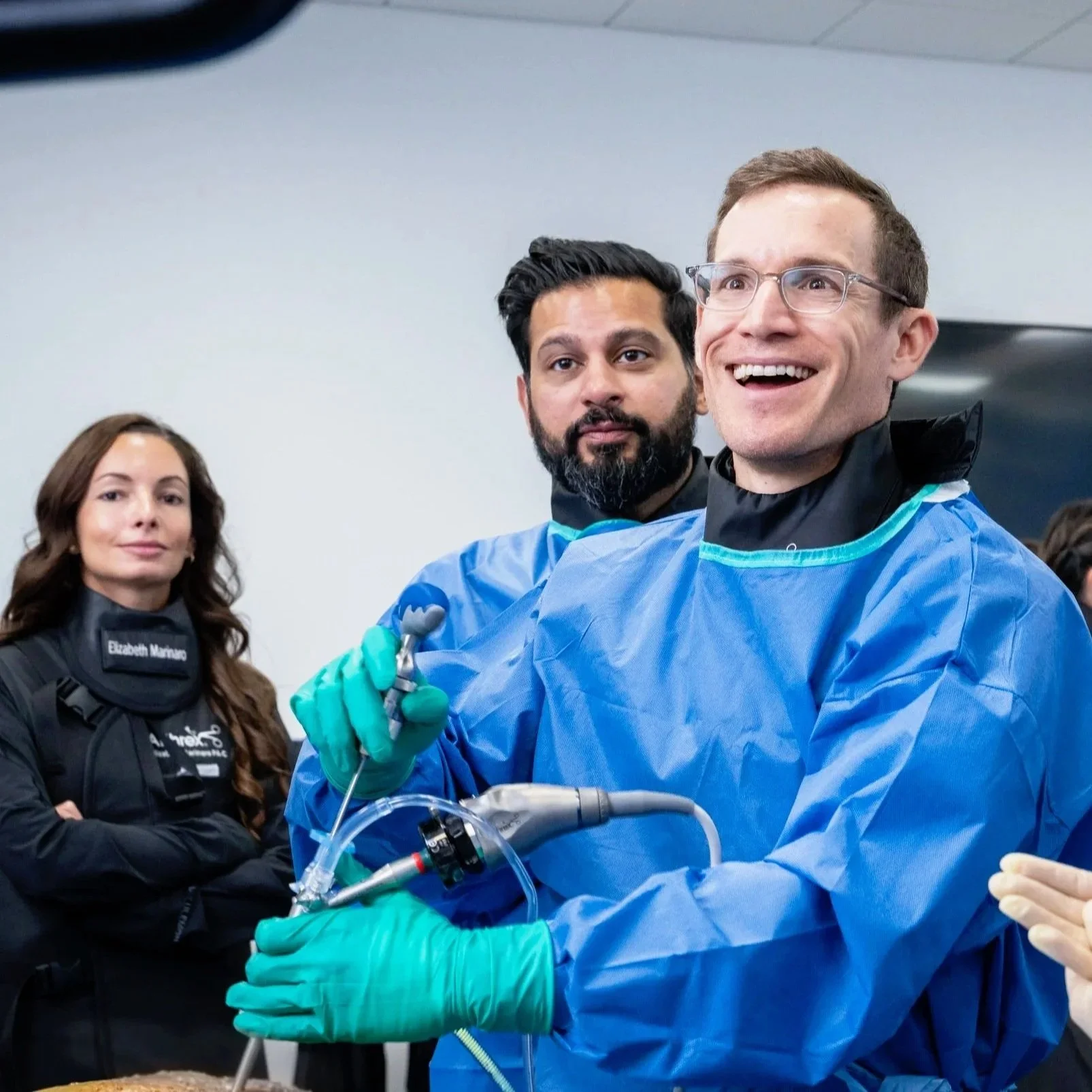 Dr. Derman demonstrating endoscopic spine surgery techniques to others at a course. He is wearing a surgical gown and gloves and smiling as others observe.
