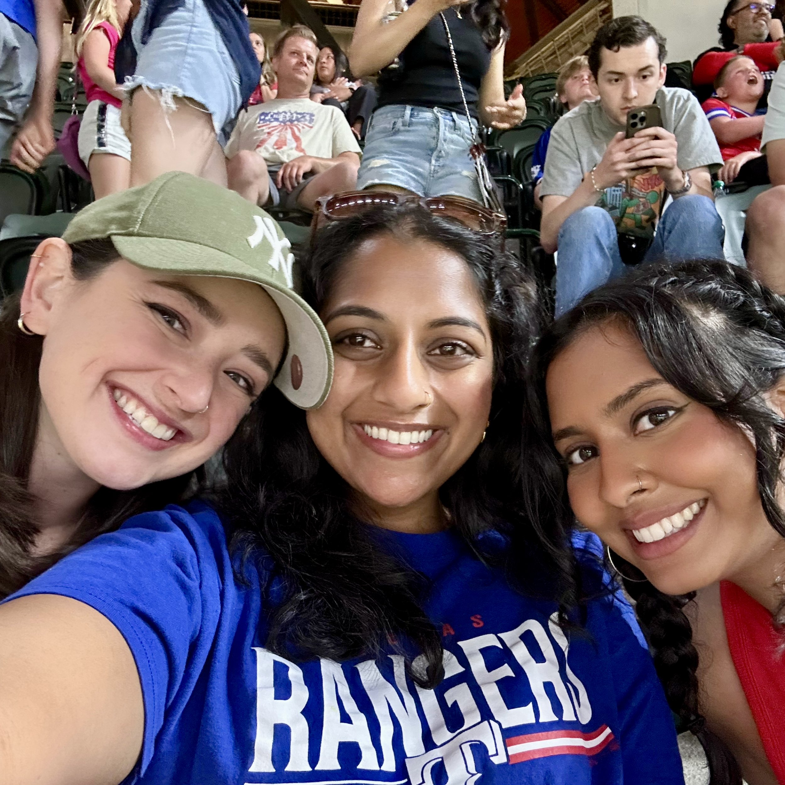 Close-up of Claire and two female friends at a rally or event, with some wearing casual clothing and showing excitement or focus, and one person wearing a blue shirt with partially visible red, white, and blue text.