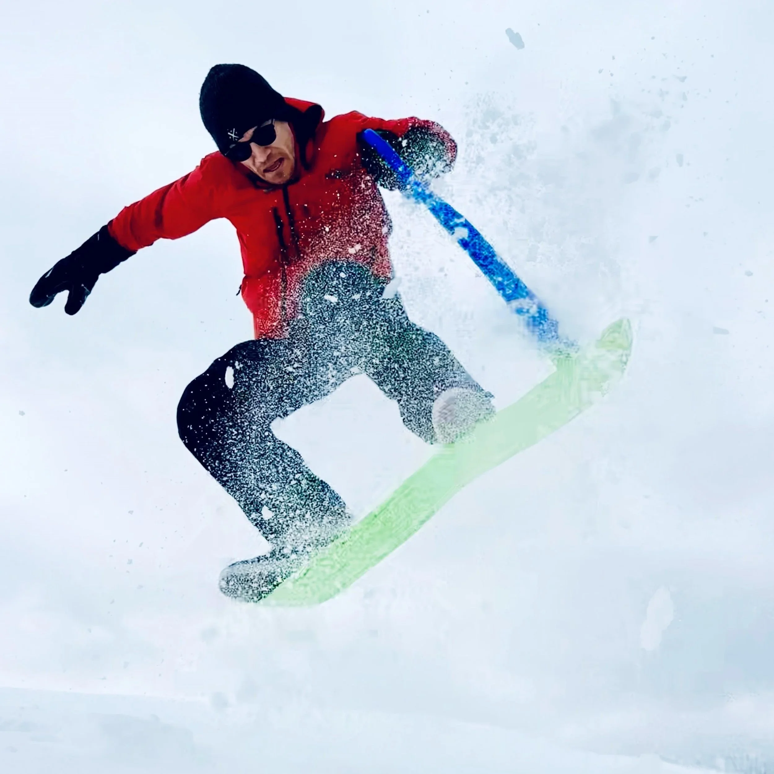 Dr. Derman jumping on a stand-up sled on snowy mountain, wearing red jacket, black pants, sunglasses, and a black beanie.