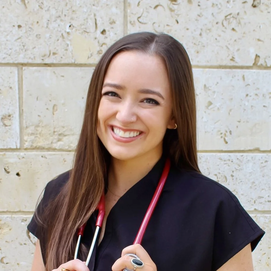 Claire Nagel, PA smiling with long brown hair, wearing a black top and a stethoscope around her neck, standing against a beige brick wall.