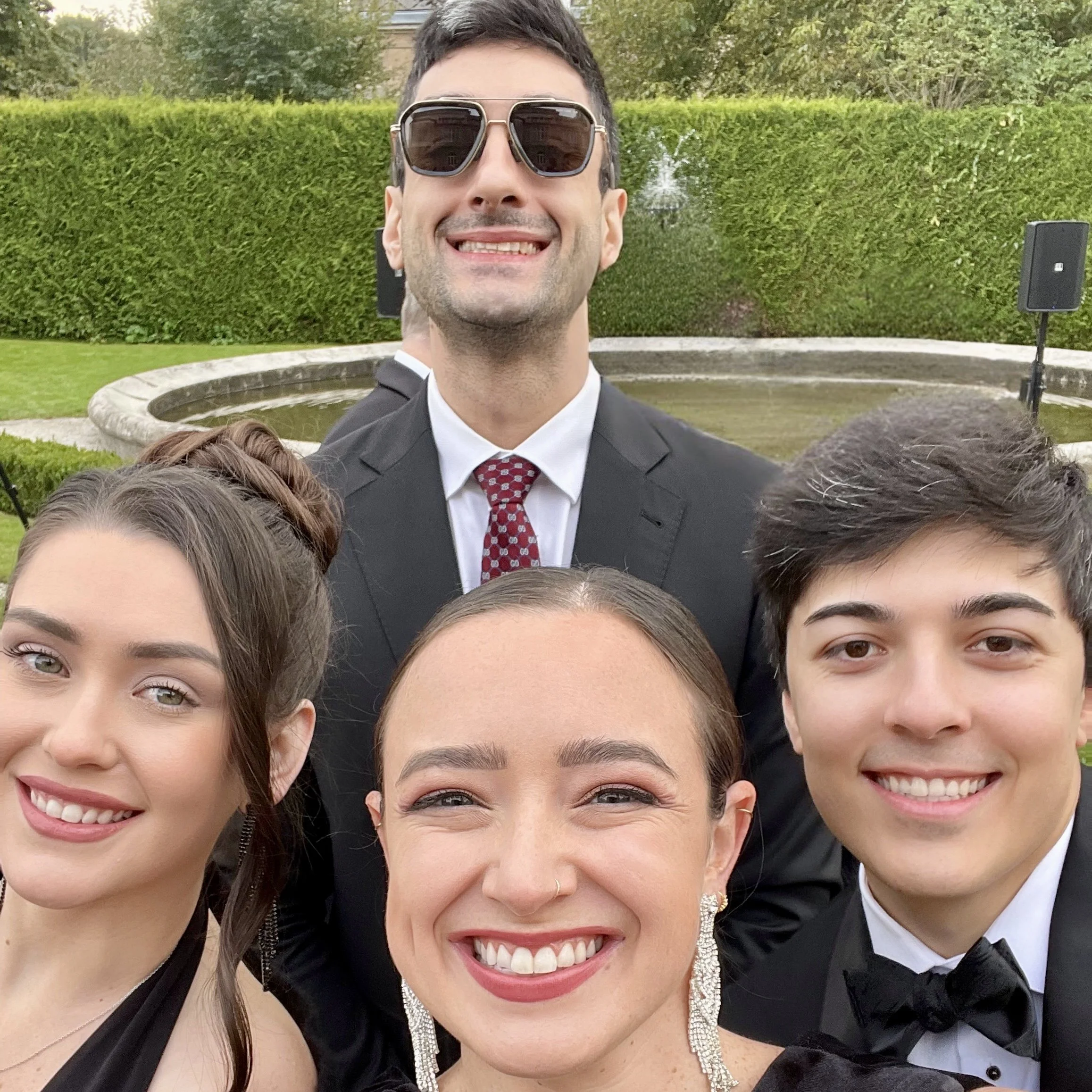 Close-up of Claire, her boyfriend, and two other friends in formal attire. They are smiling outside with greenery in the background.