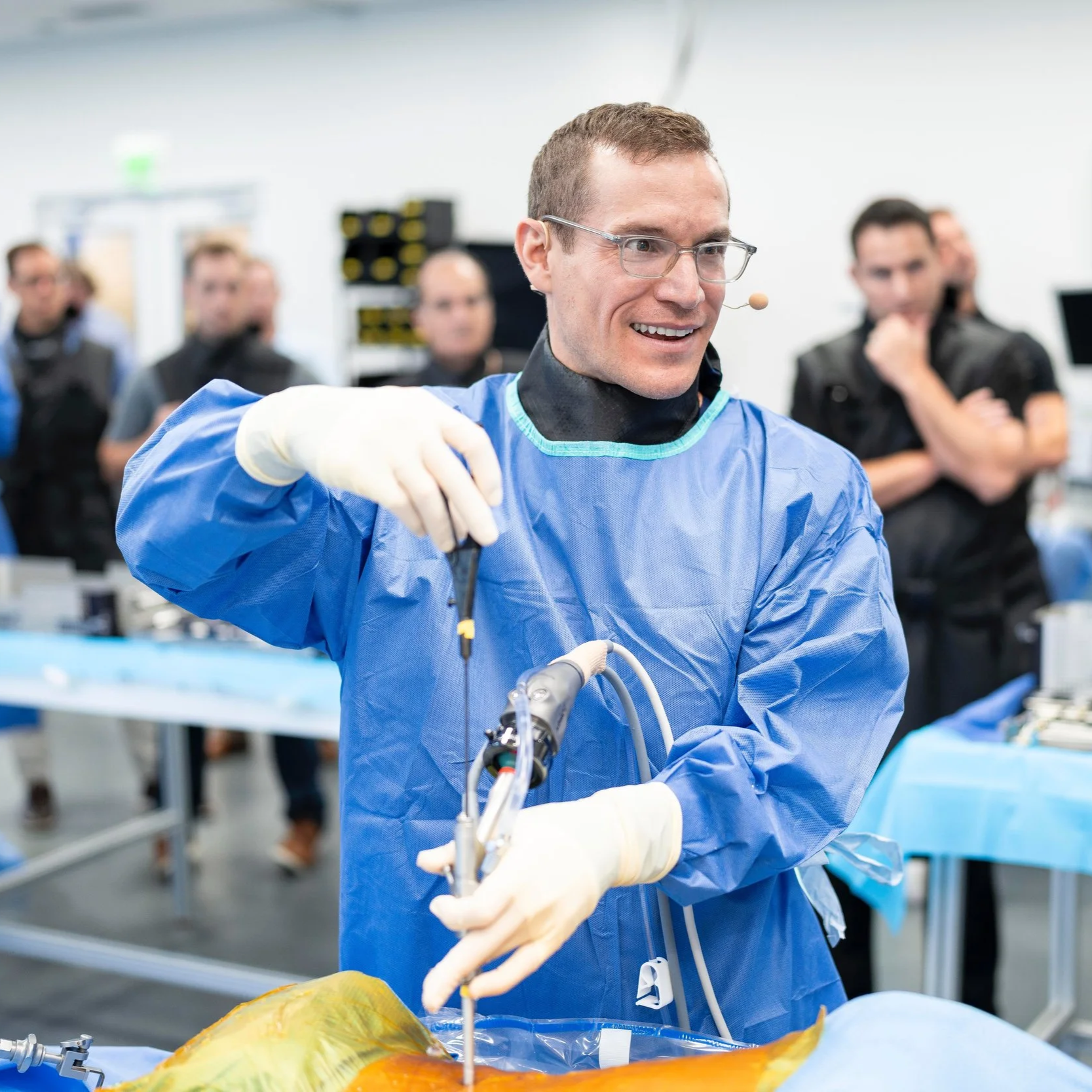 Dr. Derman demonstrating endoscopic spine surgery techniques. Other surgeons in the background are observing him. Surgical equipment is present.