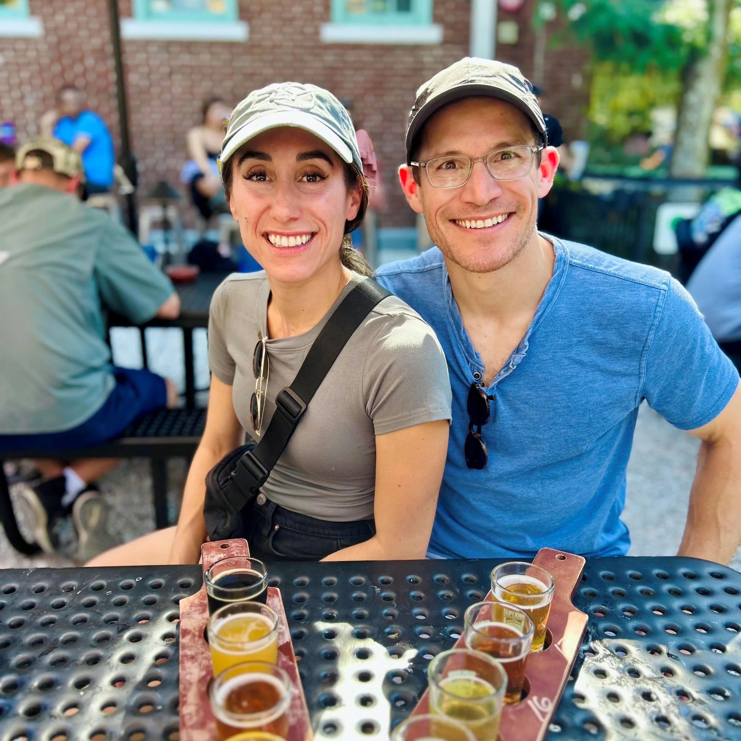 Close-up of Dr. Derman and his wife on a sunny day at a picnic table with beer flights.