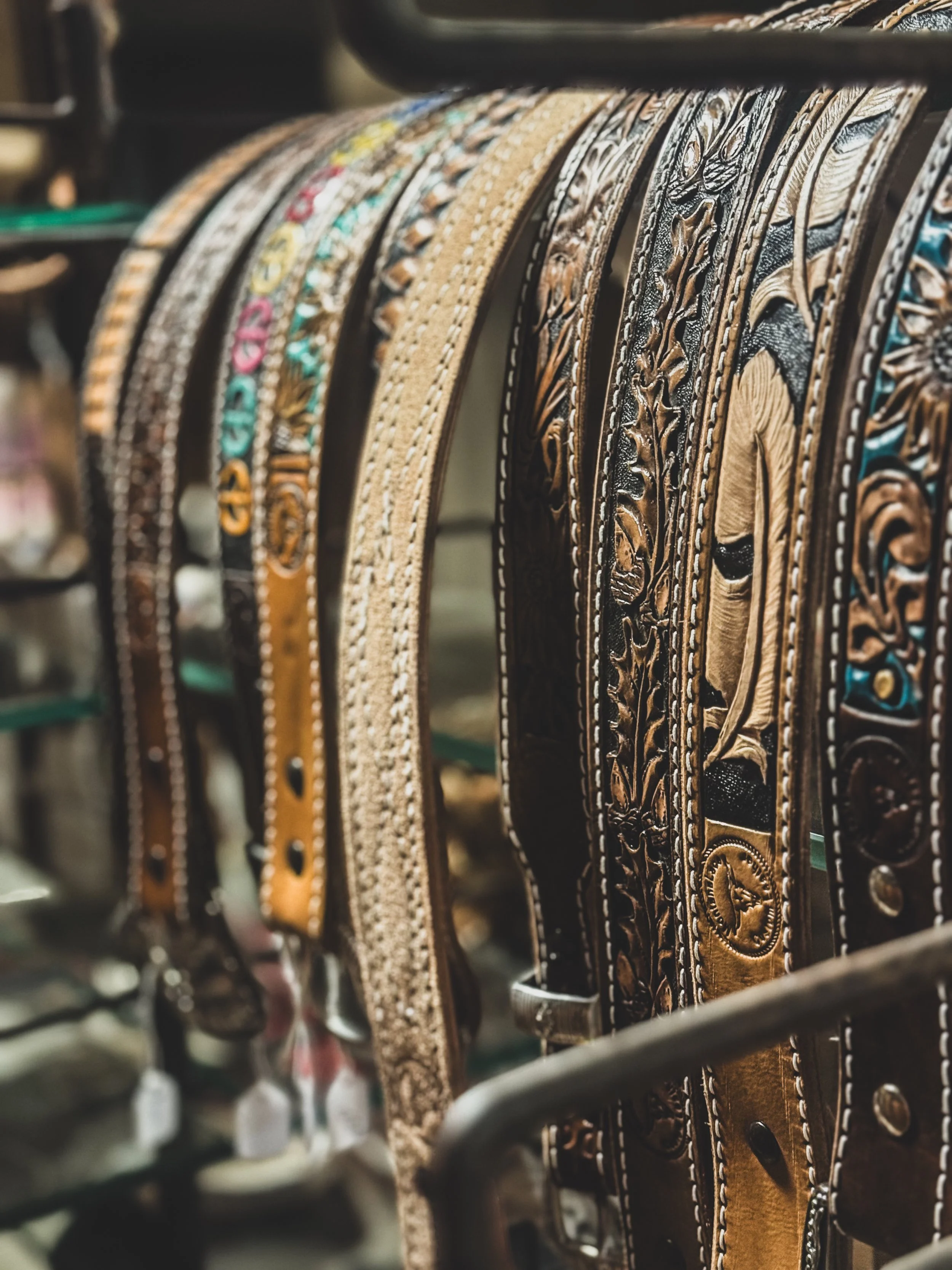 Close-up of various leather belts with decorative embossing and stitching hanging on a rack.