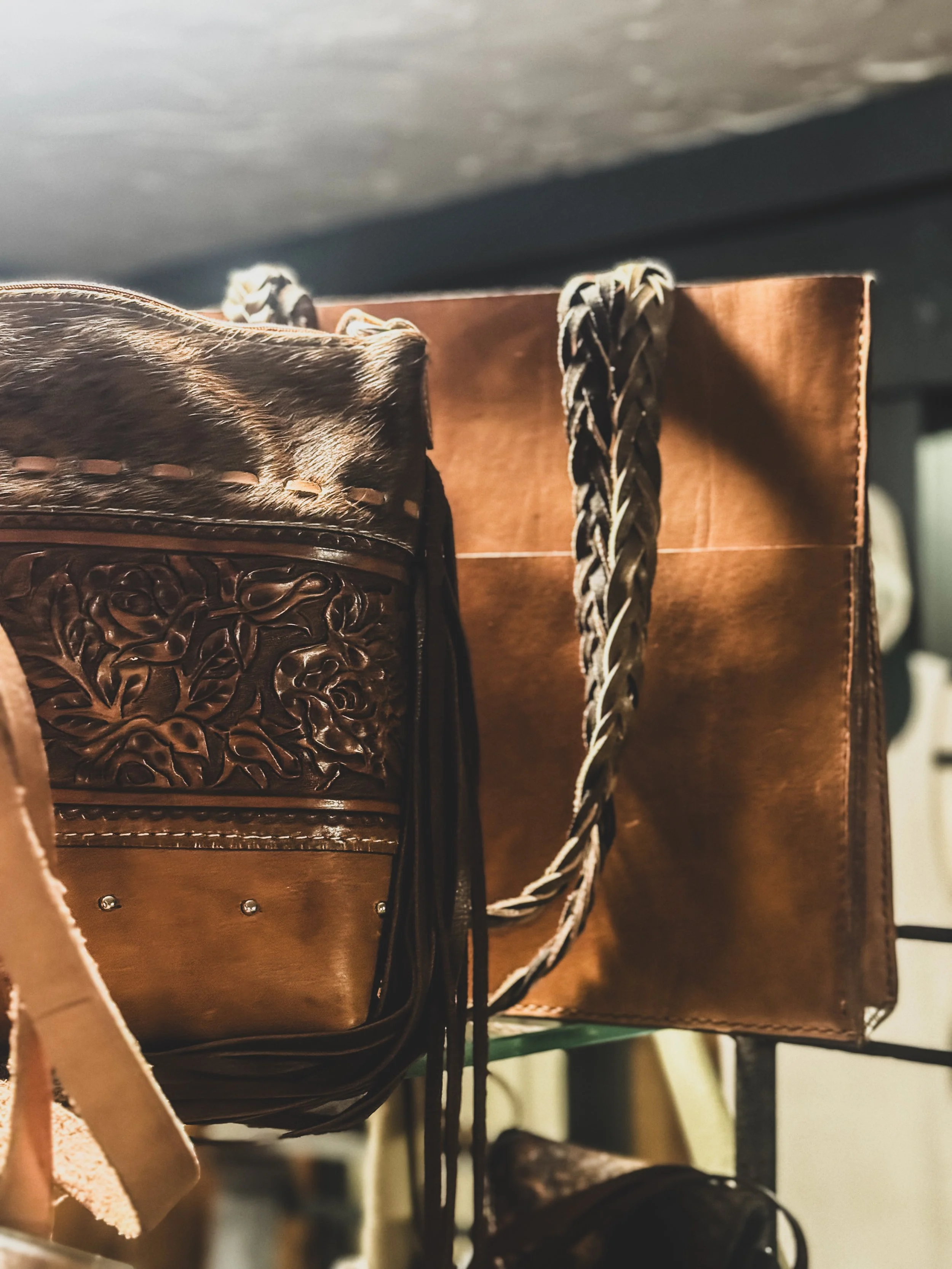 Close-up of a leather tooled handbag with elements hanging from a rack in a store.