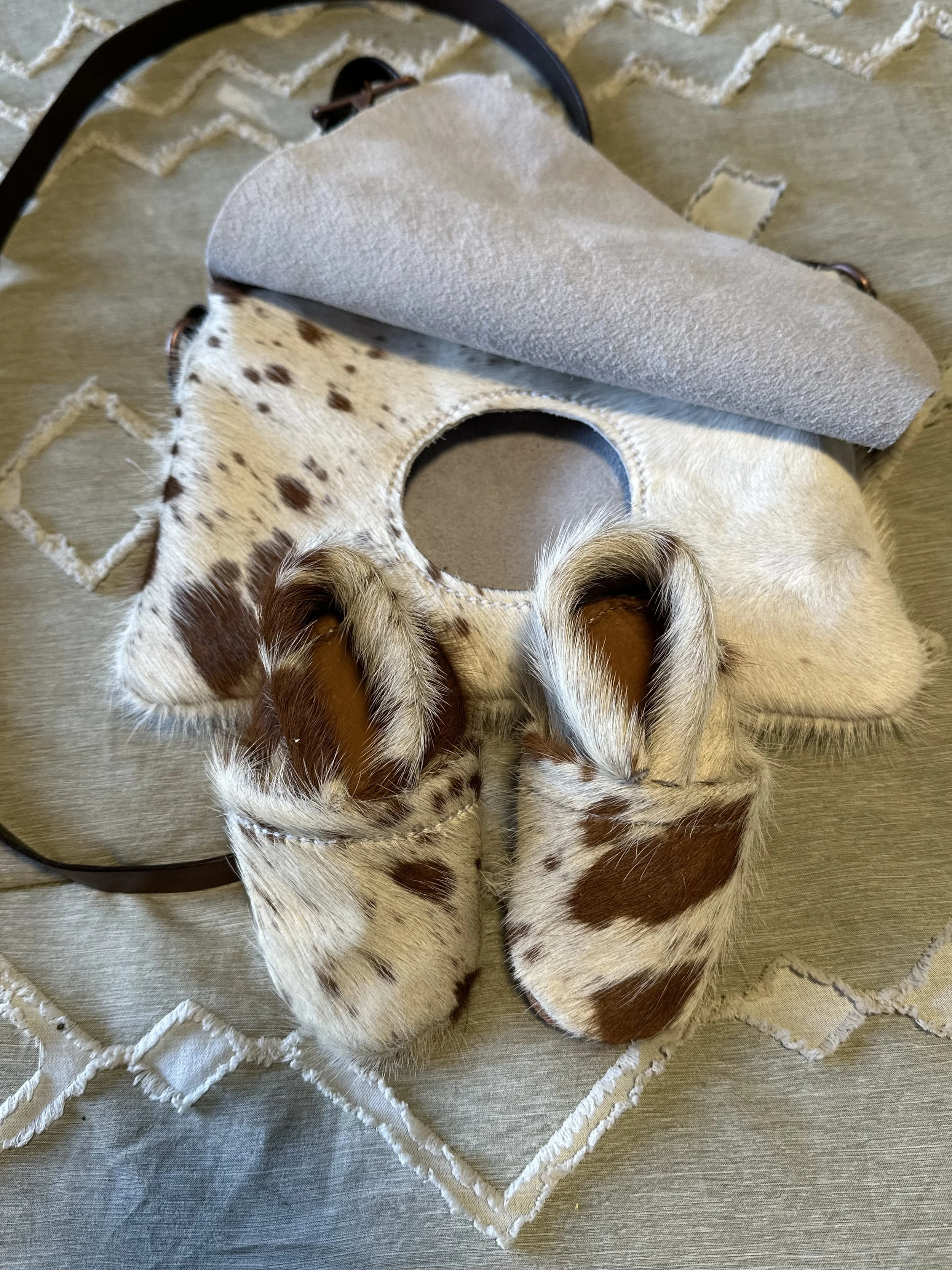 Close-up of two young spotted and brown puppies sleeping on a beige quilted fabric surface with a semi-circle scratcher or pad partially draped over one puppy.