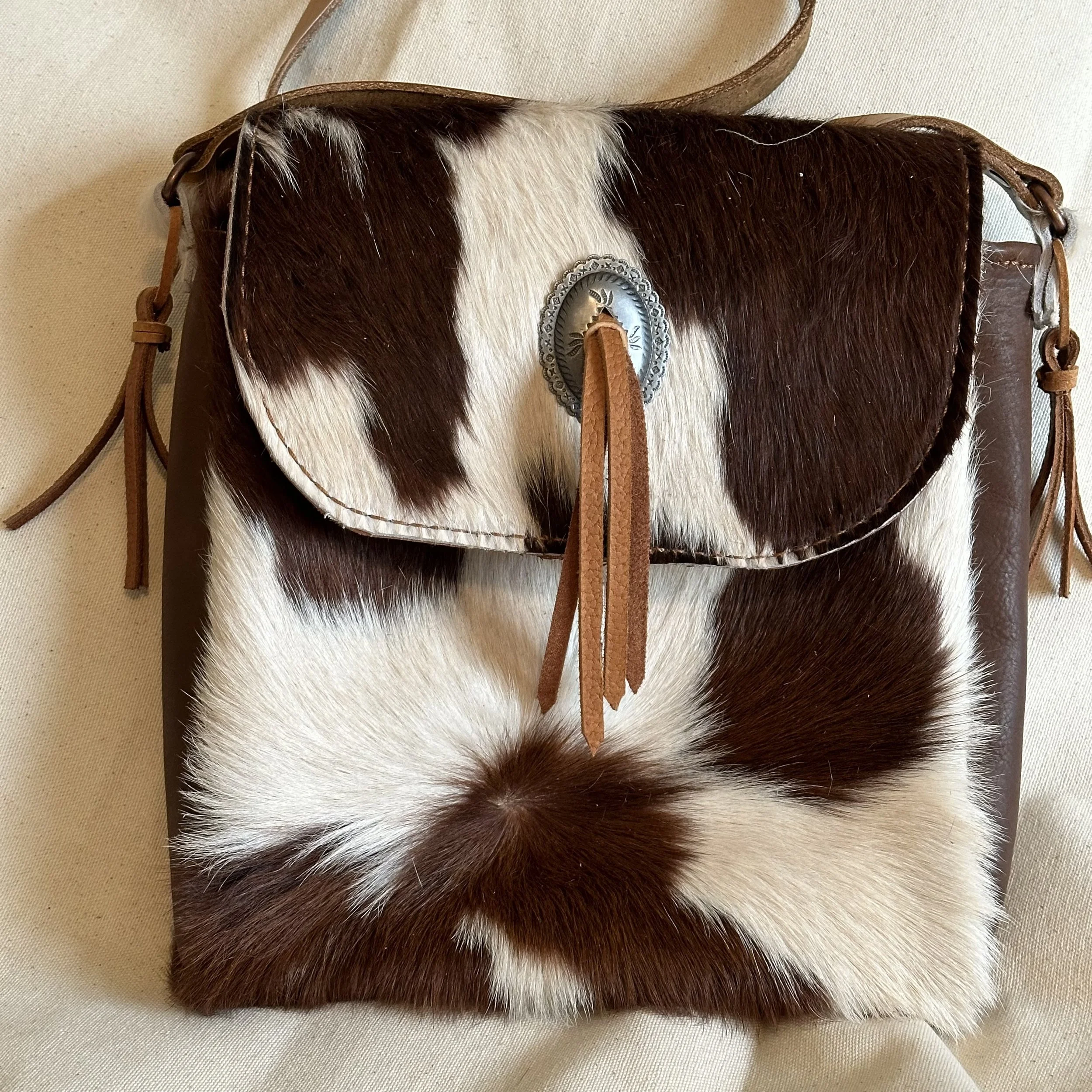A leather strap with a silver concho and a cowhide-patterned bag.