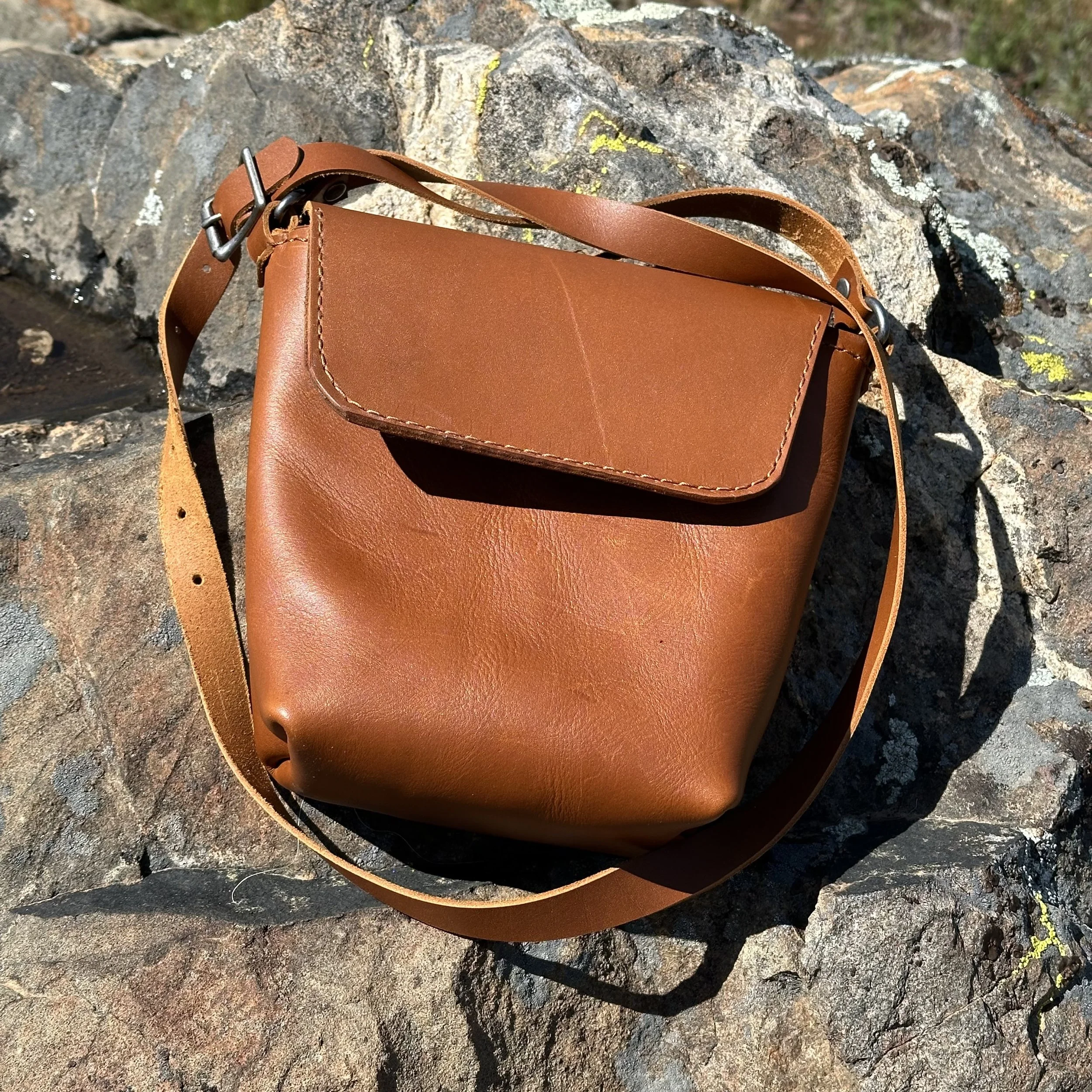 A brown leather handbag resting on a rocky surface outdoors.
