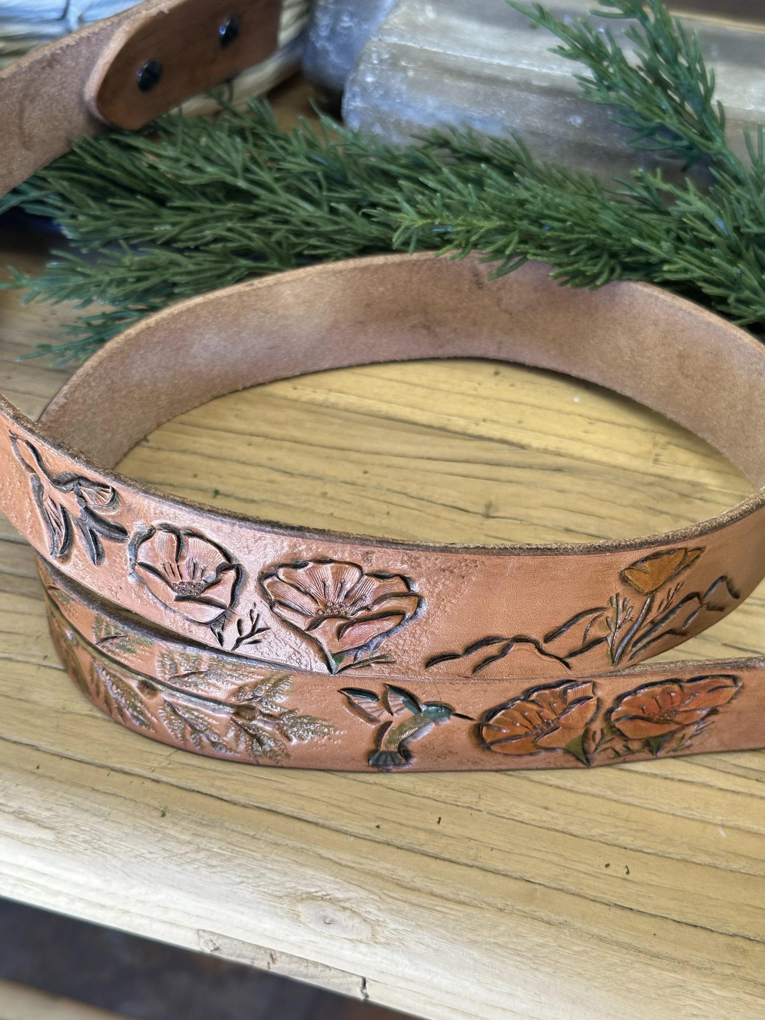 A decorative wooden container with detailed carvings of flowers and leaves, containing green artificial pine branches, placed on a wooden surface.