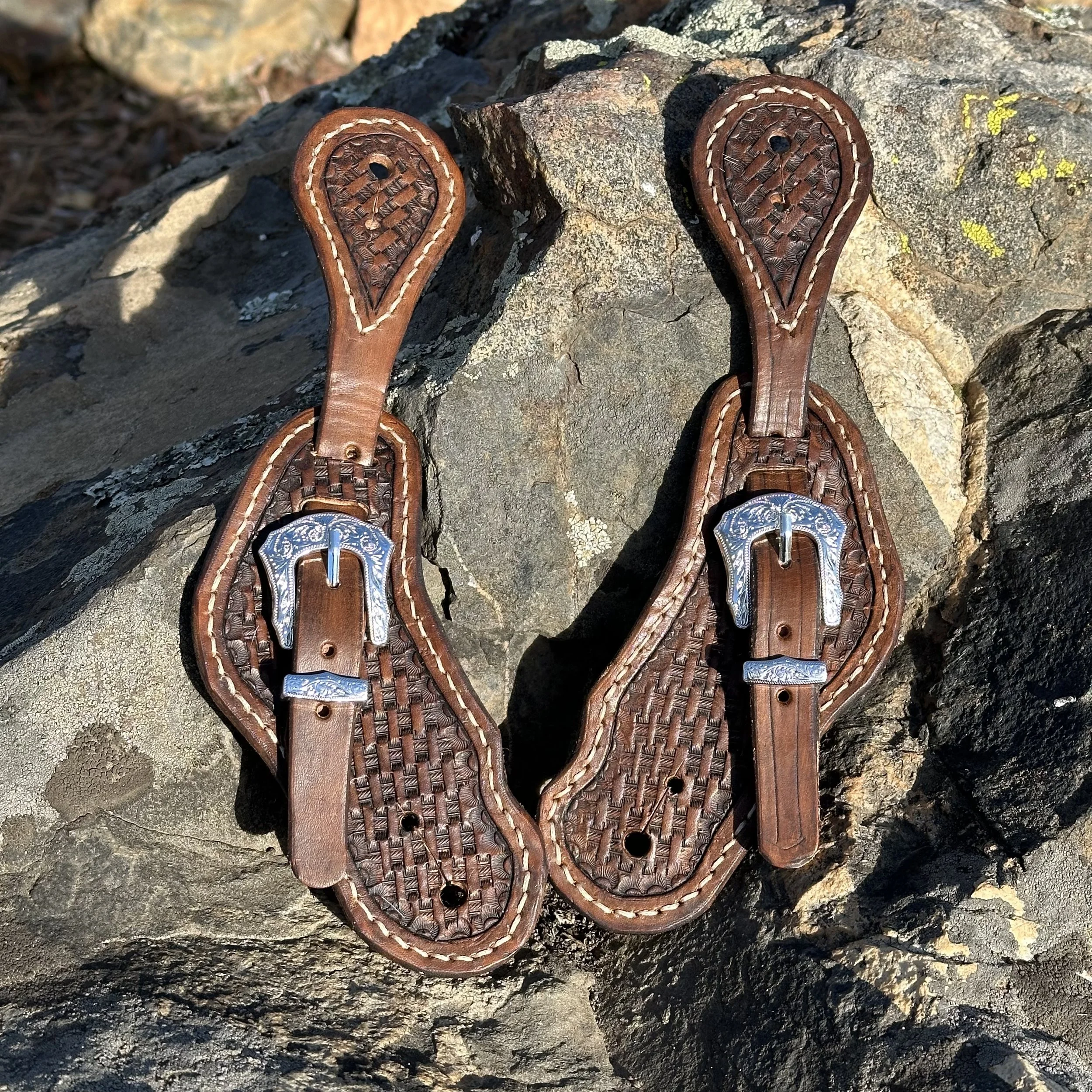 Pair of leather sandals with woven pattern and silver embellishments on rocky terrain.