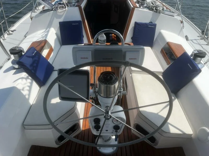 View of a boat's cockpit with a steering wheel, navigation screens, and seating with blue cushions.