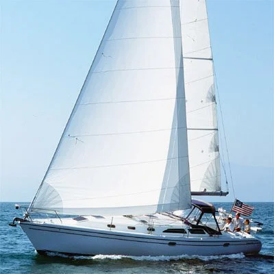 A sailboat with white sails on the water, with two people on board, flying an American flag, under a clear blue sky.