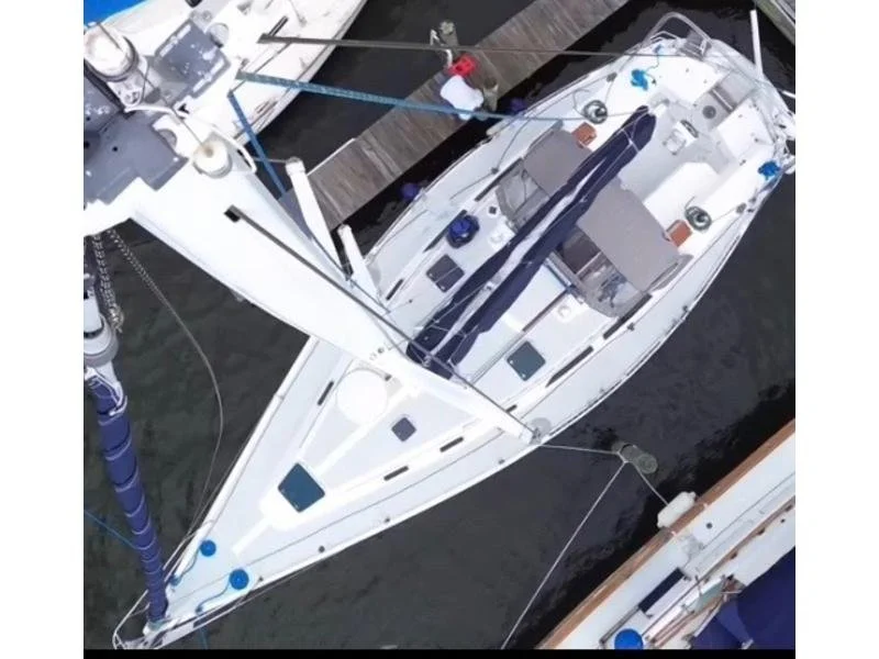 A white sailboat docked at a marina seen from above, with various ropes, equipment, and a small sail cover on the deck.