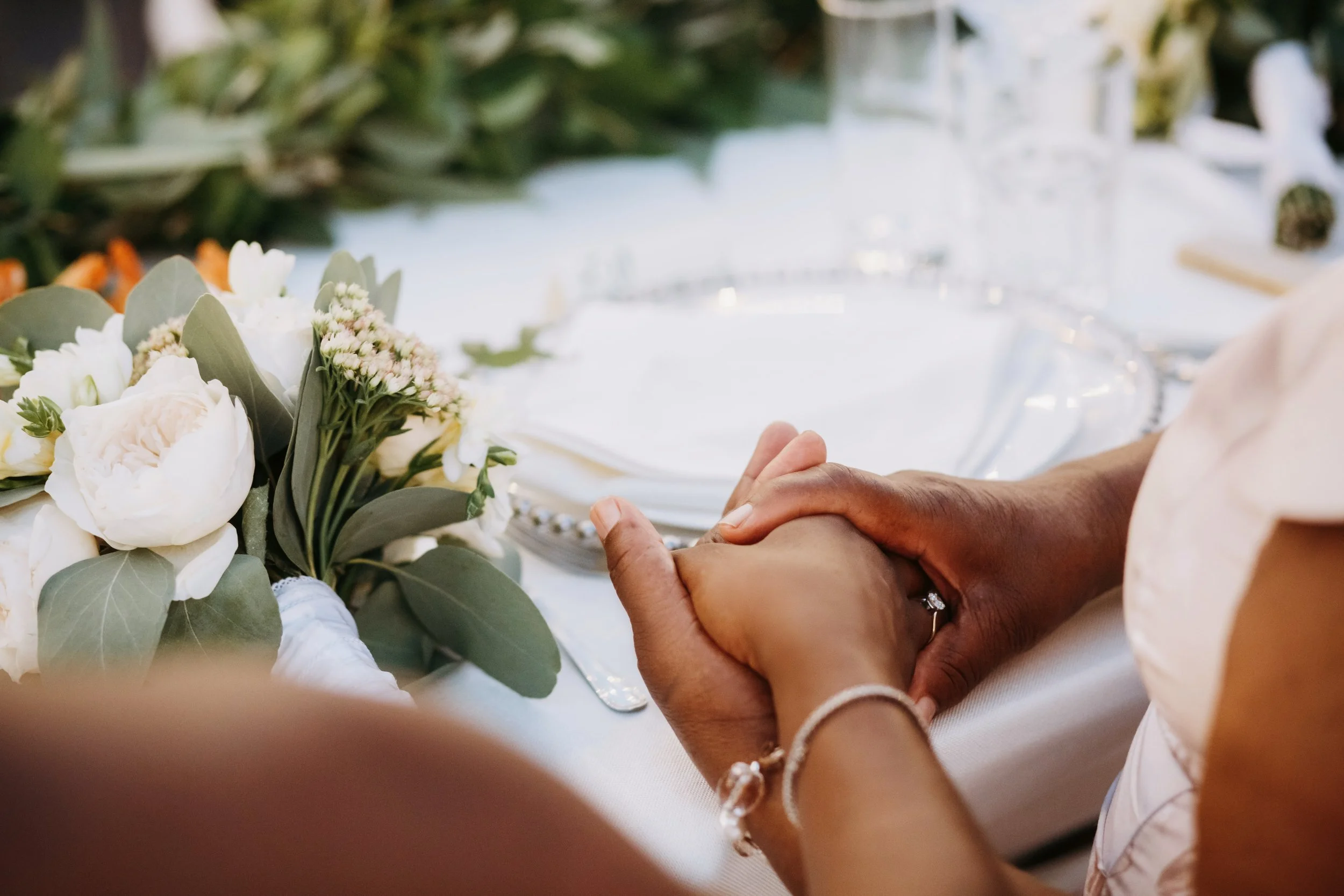 Deux personnes tenant leurs mains ensemble lors d'une cérémonie de mariage, avec des fleurs blanches et vertes en décoration.