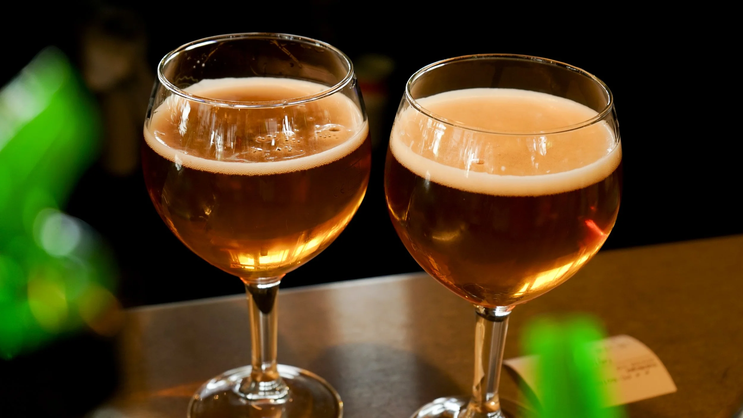 Deux verres à vin remplis de champagne ou de vin mousseux, posés sur une surface en bois, avec un fond sombre et des lumières floues.