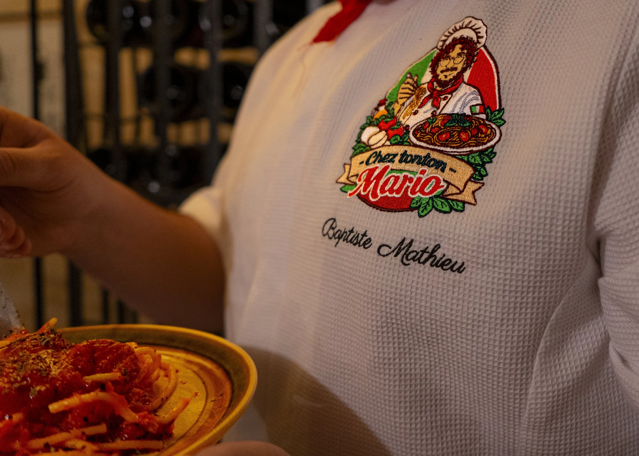 Vêtements portant une broderie d'un chef italien avec une assiette de spaghettis à la sauce tomate. Broderie mentionne 'Chez tonton Mario' et 'Capitaine M