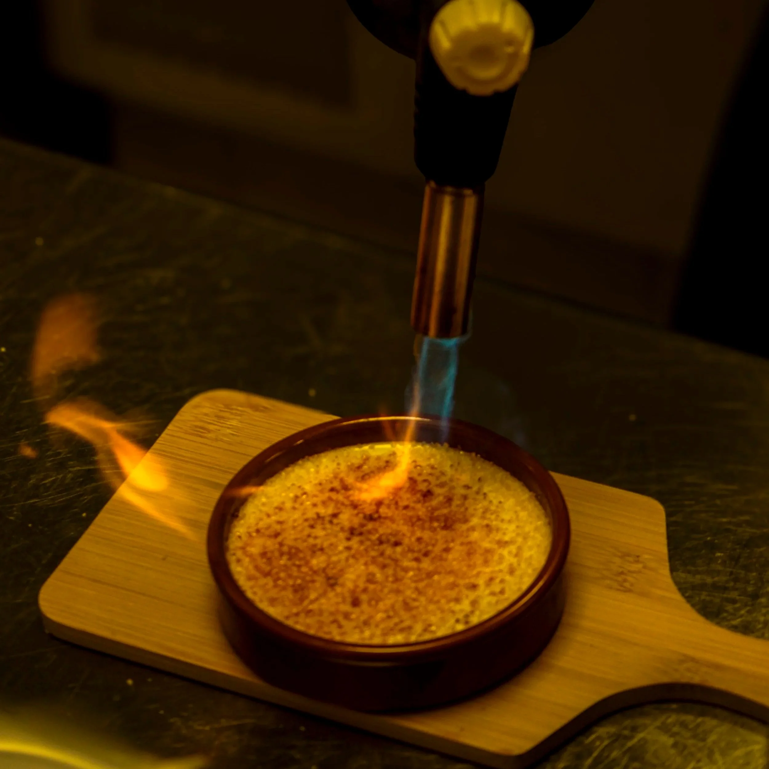 Un brûleur à tabac allumé avec une flamme bleue, placé sur une surface en bois, avec une poudre arôme dans un bol en cuivre.