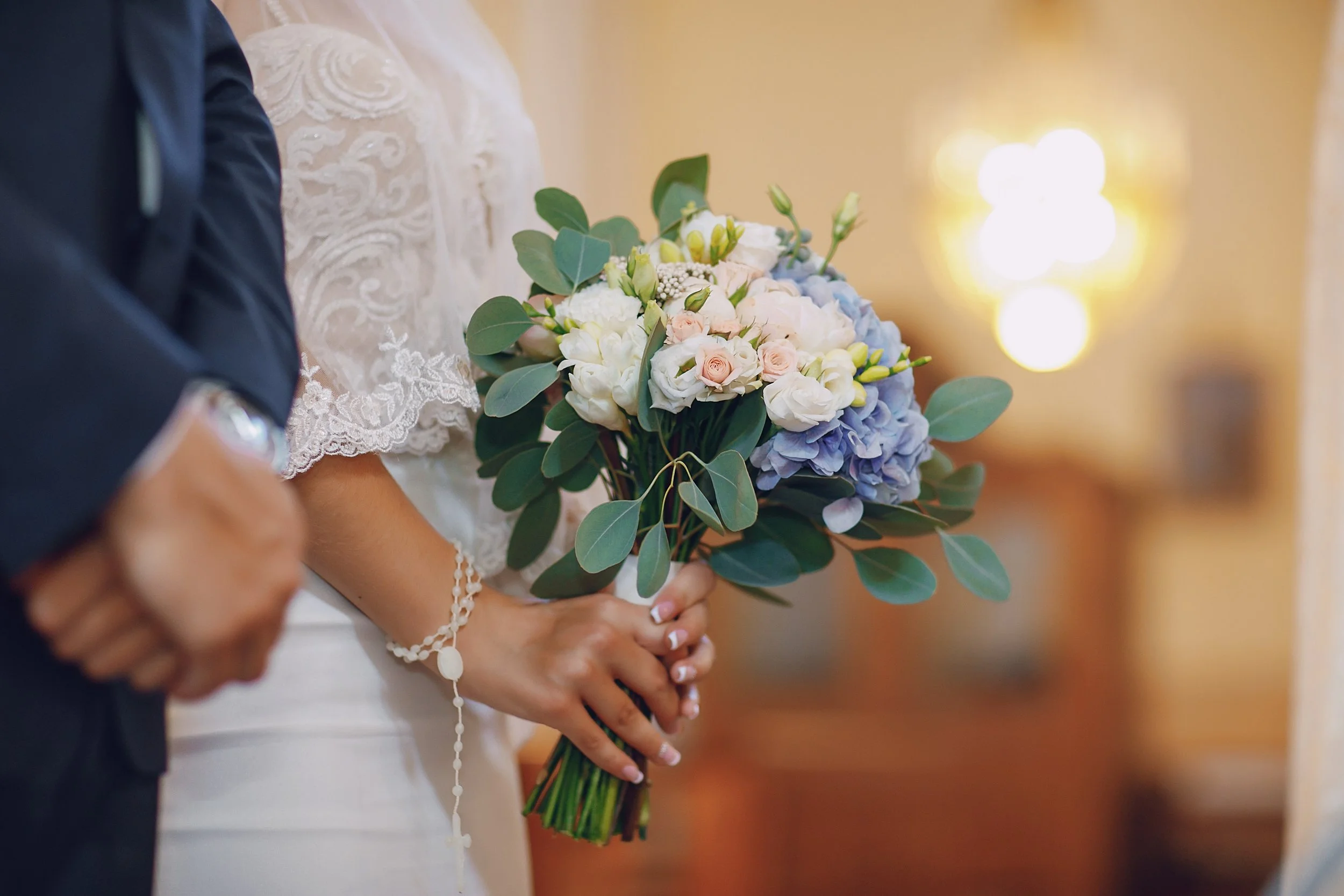 Une mariée tenant un bouquet de fleurs avec des roses, des lys blancs, des hortensias bleus et des feuilles vertes, lors d'un mariage.