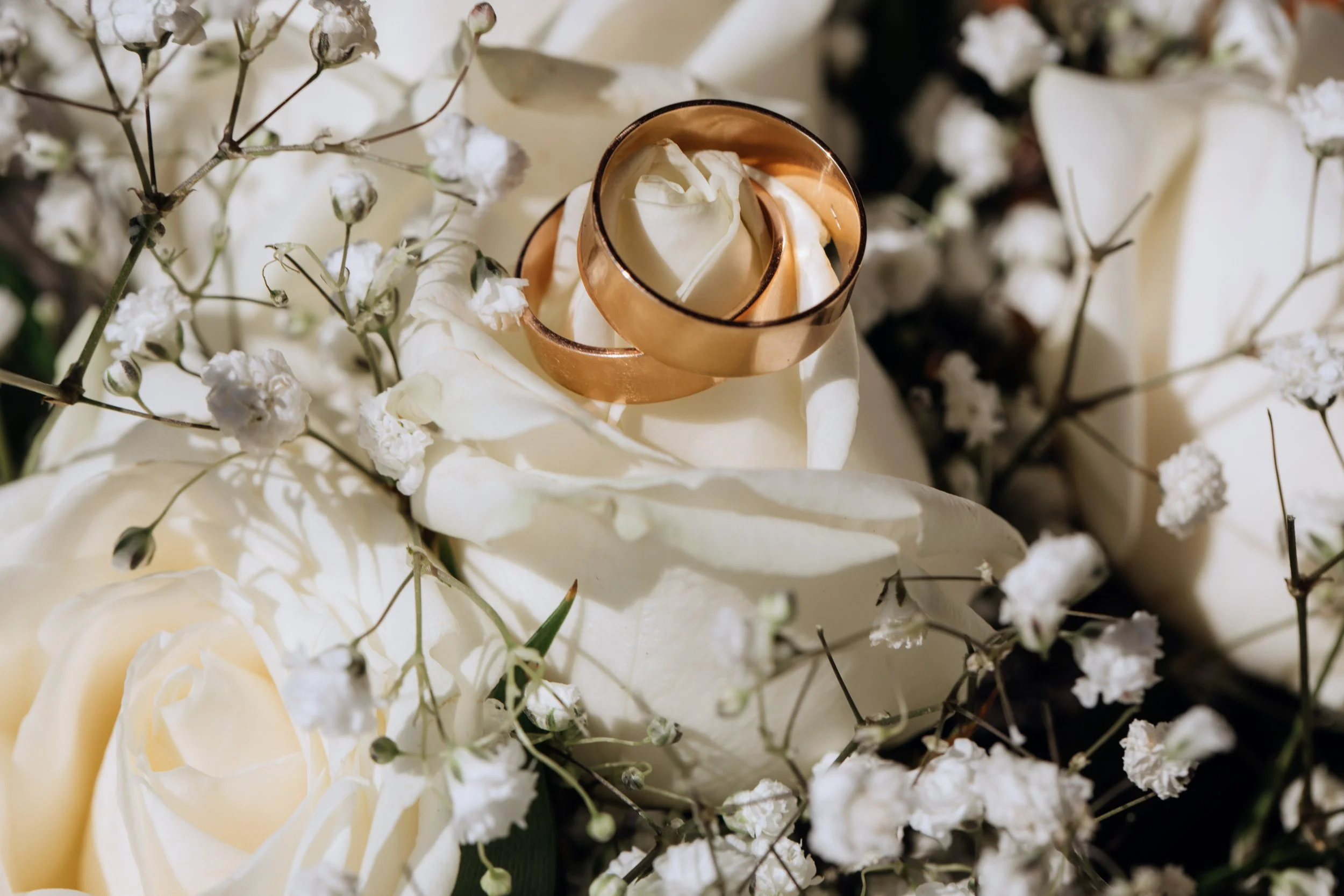 Une bougie blanche dans un support en cuivre, entourée de fleurs blanches, dont des roses et des gypsophiles.