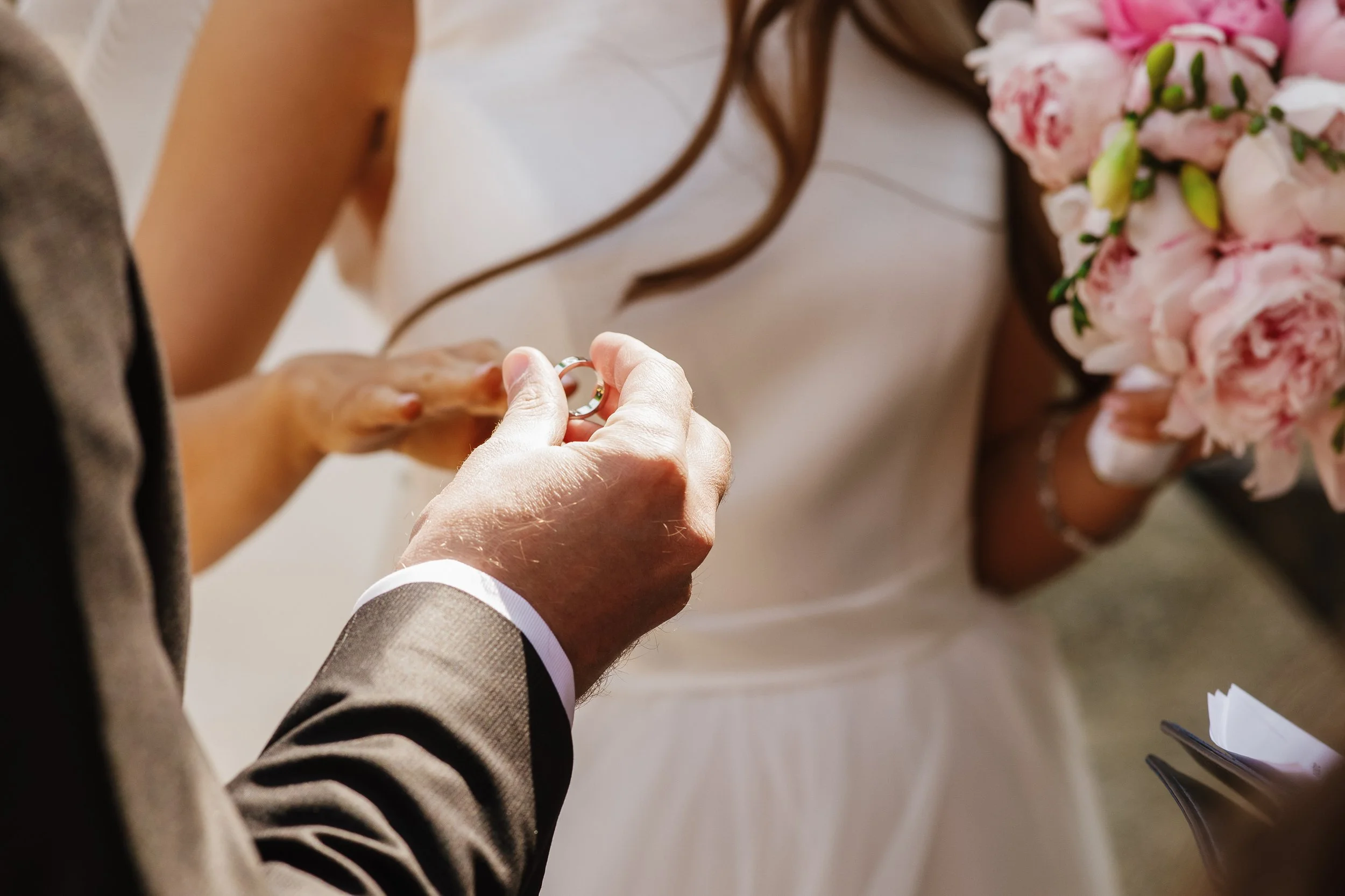 Un homme en costume gris offre une bague à une femme vêtue d'une robe blanche lors d'une cérémonie de mariage.