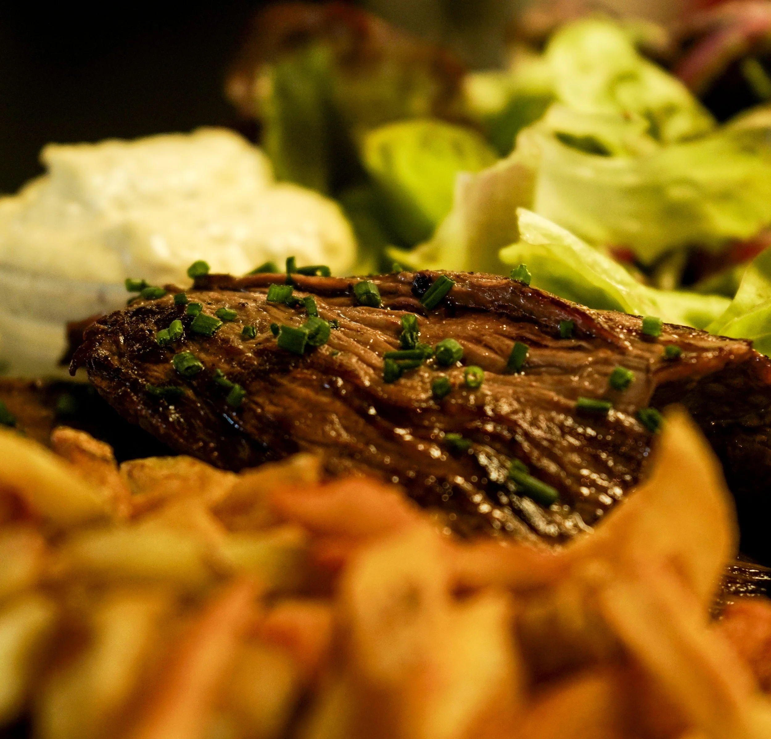 Une brochette de viande grillée garnie de ciboulette, avec une salade verte et une sauce blanche en accompagnement, le tout présenté sur une assiette.