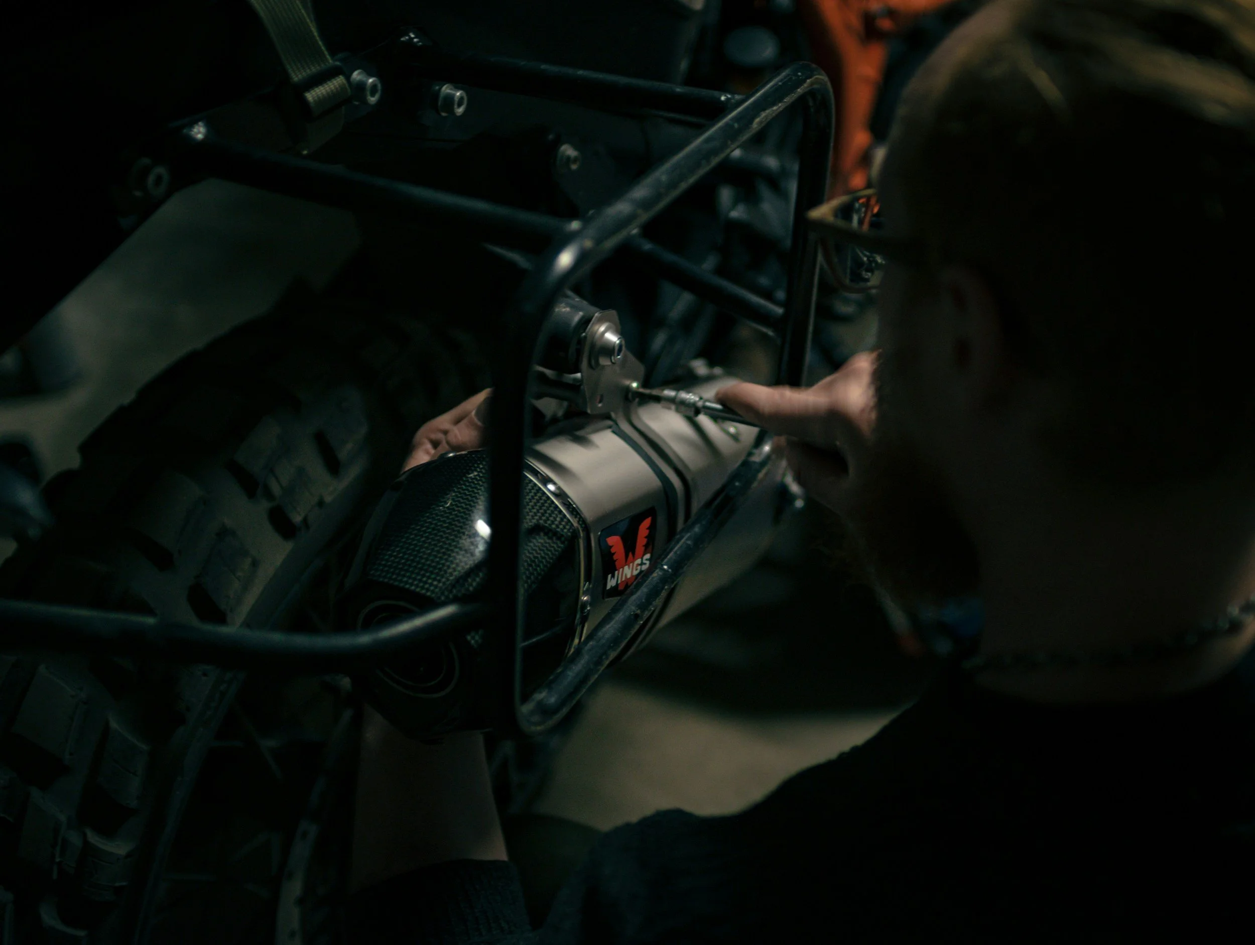 Close-up of a person working on a piece of machinery, possibly an aircraft or vehicle, in a dimly lit environment.