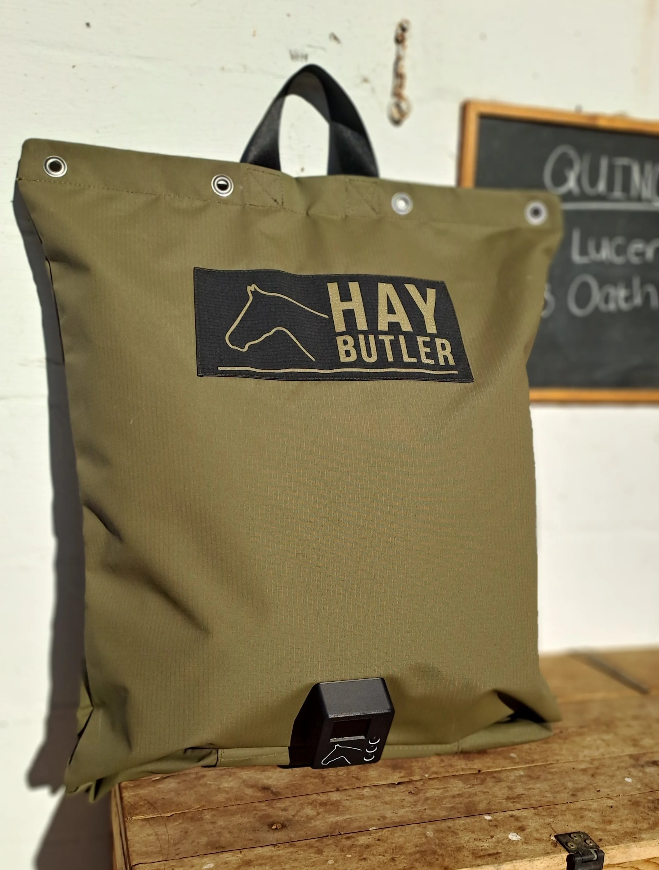 A khaki-colored bag with black handles and grommet holes, featuring a logo of a horse's head and the brand name 'HAY BUTLER' on a black patch.