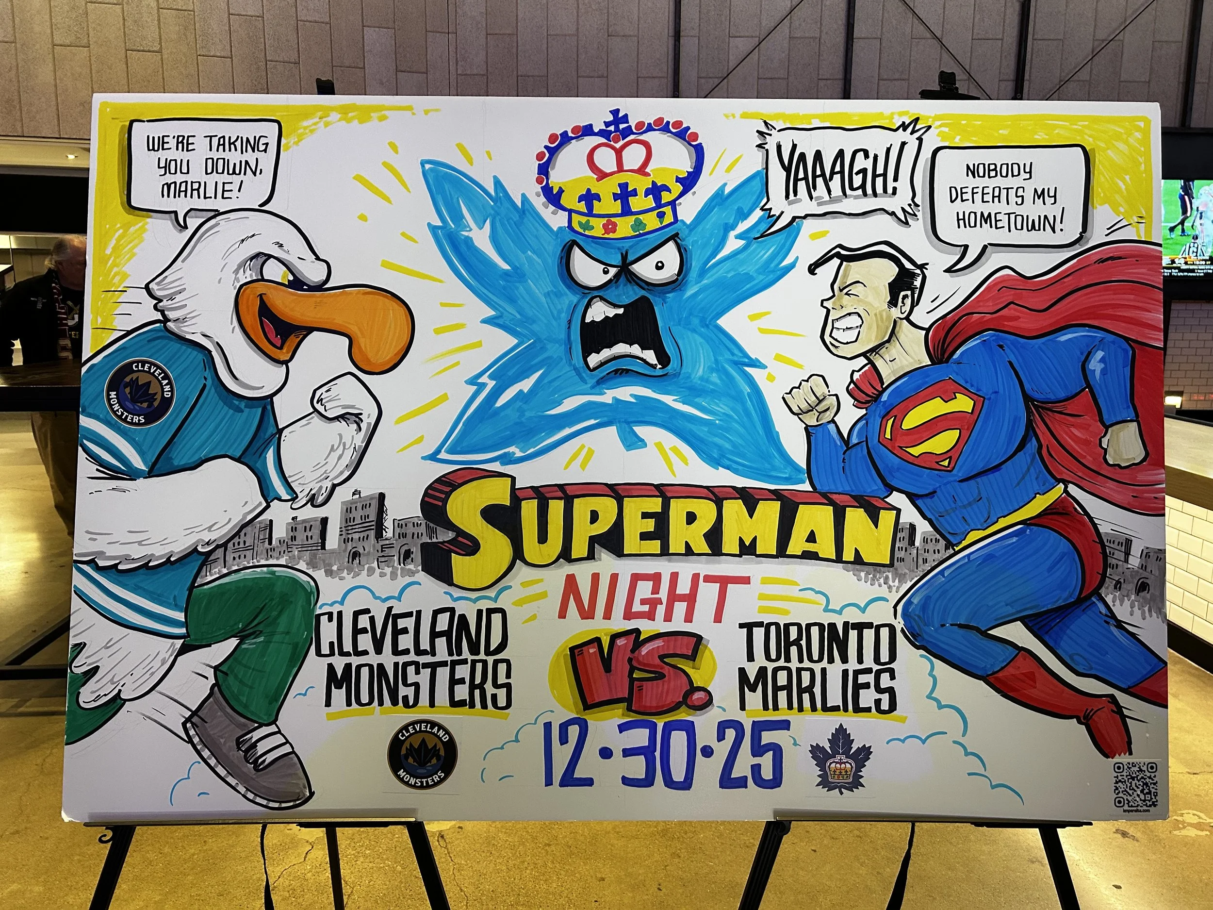 A colorful comic-style poster depicting Superman and a character with a bird head fighting against each other, with text indicating a playful rivalry between Cleveland Monsters and Toronto Marlies hockey teams, including date and time of the event.