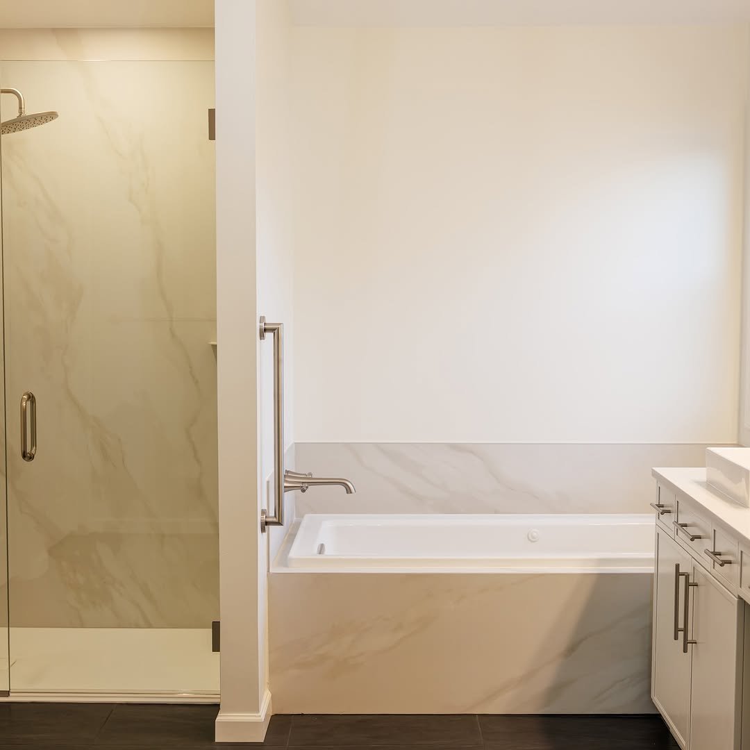 Modern bathroom featuring a glass-enclosed shower with marble walls, a built-in bathtub with marble surround, and white cabinetry with silver handles.