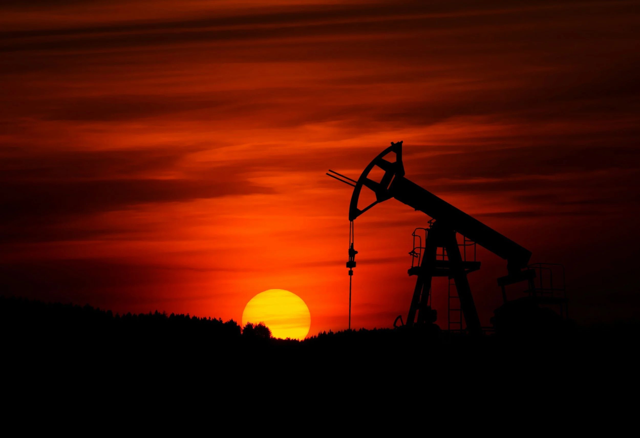 Sunset with orange and red clouds and a silhouette of an oil pumpjack in the foreground.