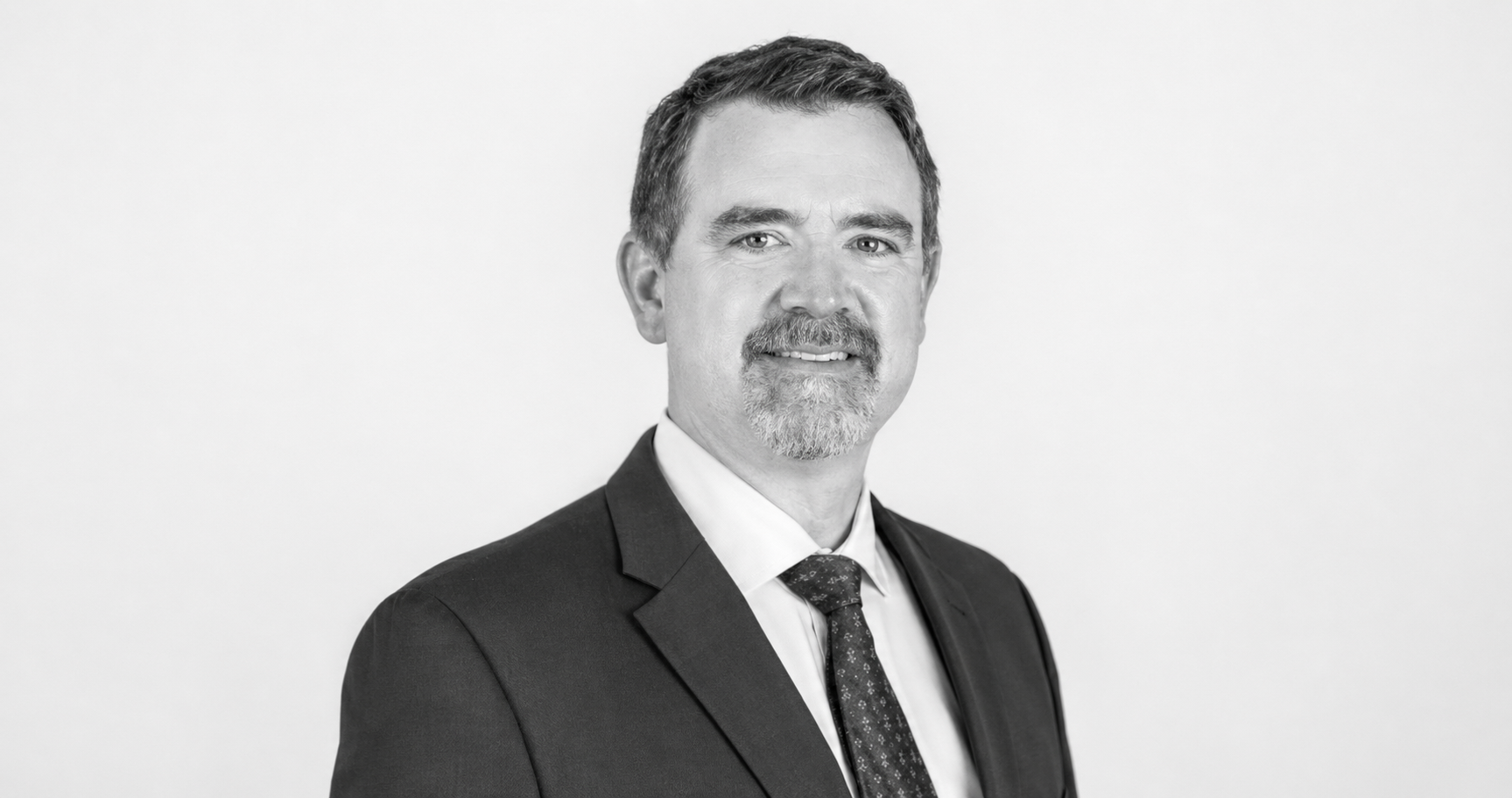Chad Valentine, Author, professional portrait of a middle-aged man with short hair, a beard, wearing a suit and tie, smiling slightly, in front of a plain background.