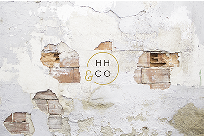 A weathered white brick wall with peeling paint, featuring a circular logo with the text 'HH & CO' in gold.