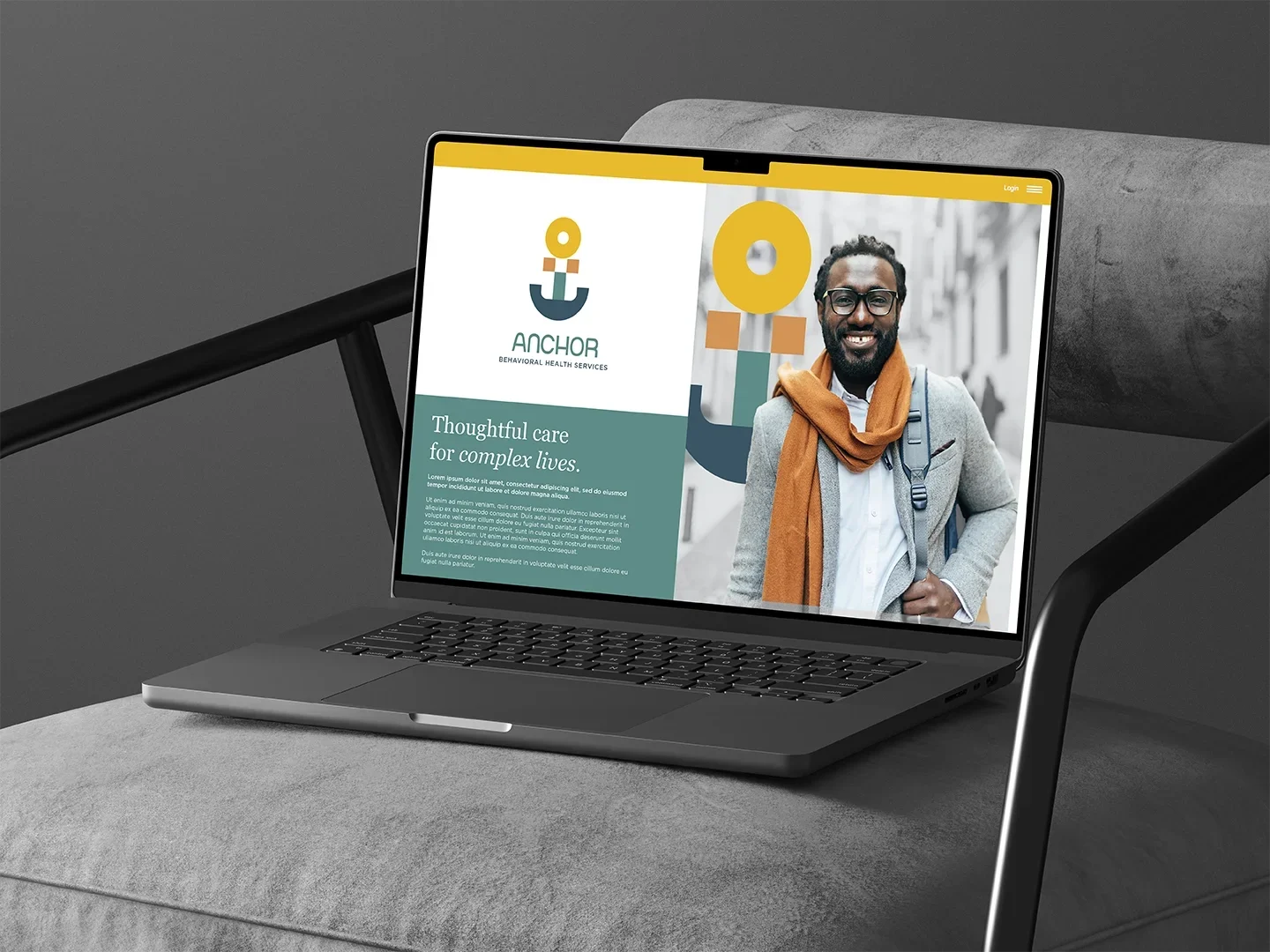 Laptop displaying a website for behavioral health services called Anchor, showing a smiling man with glasses and a backpack, outdoors on a city street.