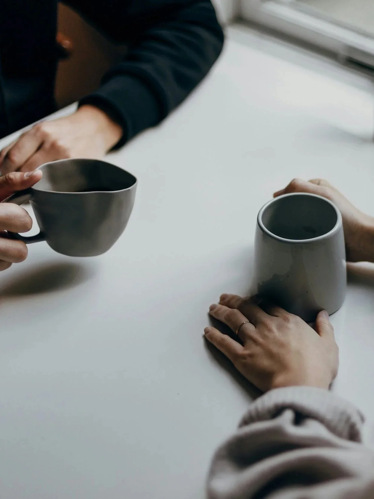 Two people exchanging coffee mugs at a white table, one person holding a gray mug and the other holding a white mug.