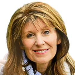 Close-up portrait of a smiling woman with shoulder-length light brown hair and bangs, wearing a light blue collared shirt.