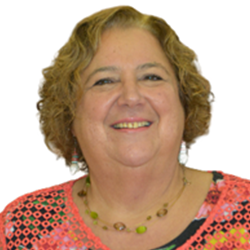 Portrait of a smiling woman with curly blonde hair, wearing a colorful patterned top and a beaded necklace.